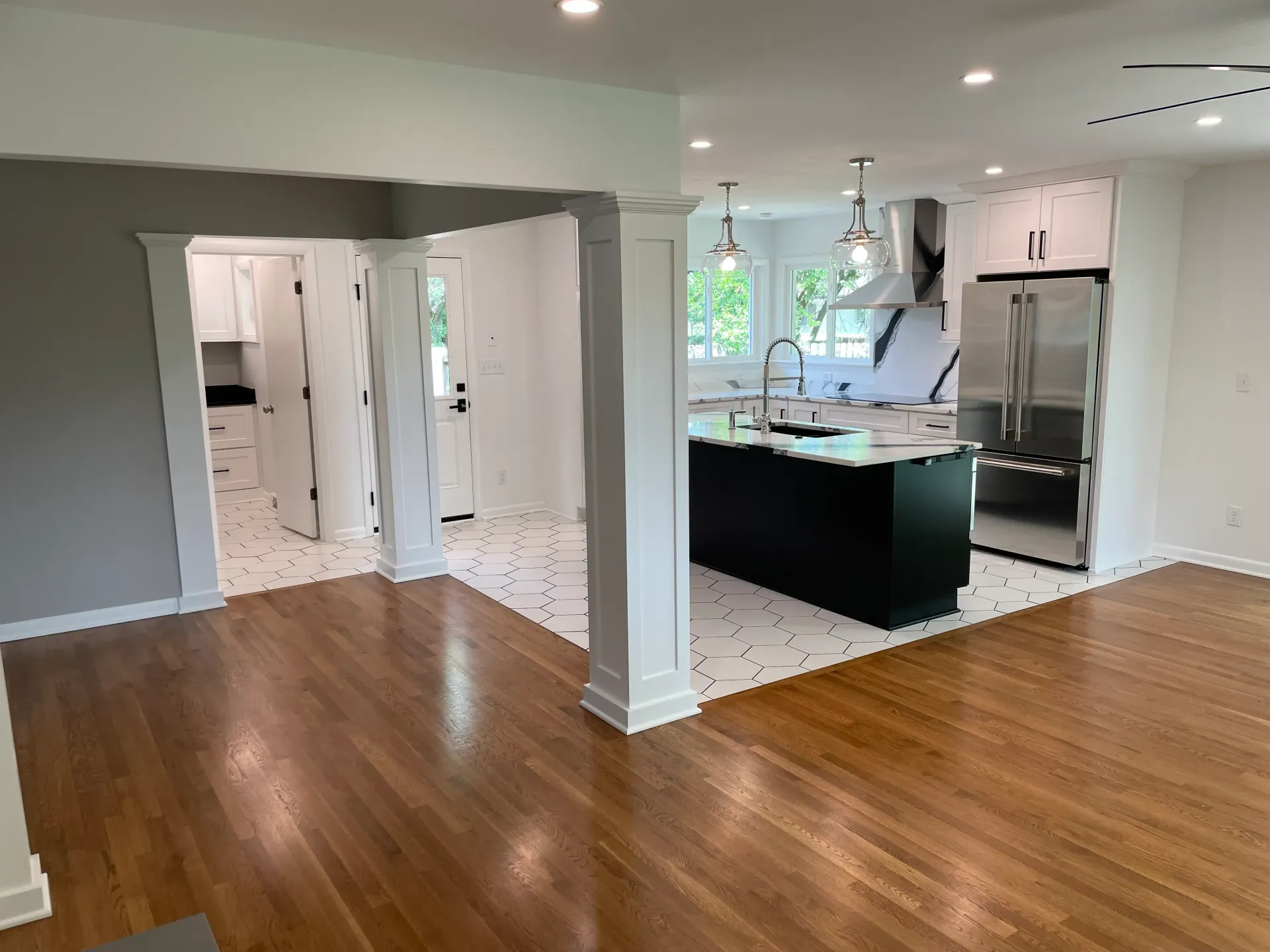 Open-concept kitchen with hardwood floors, a black island, white cabinets, and stainless steel appliances.
