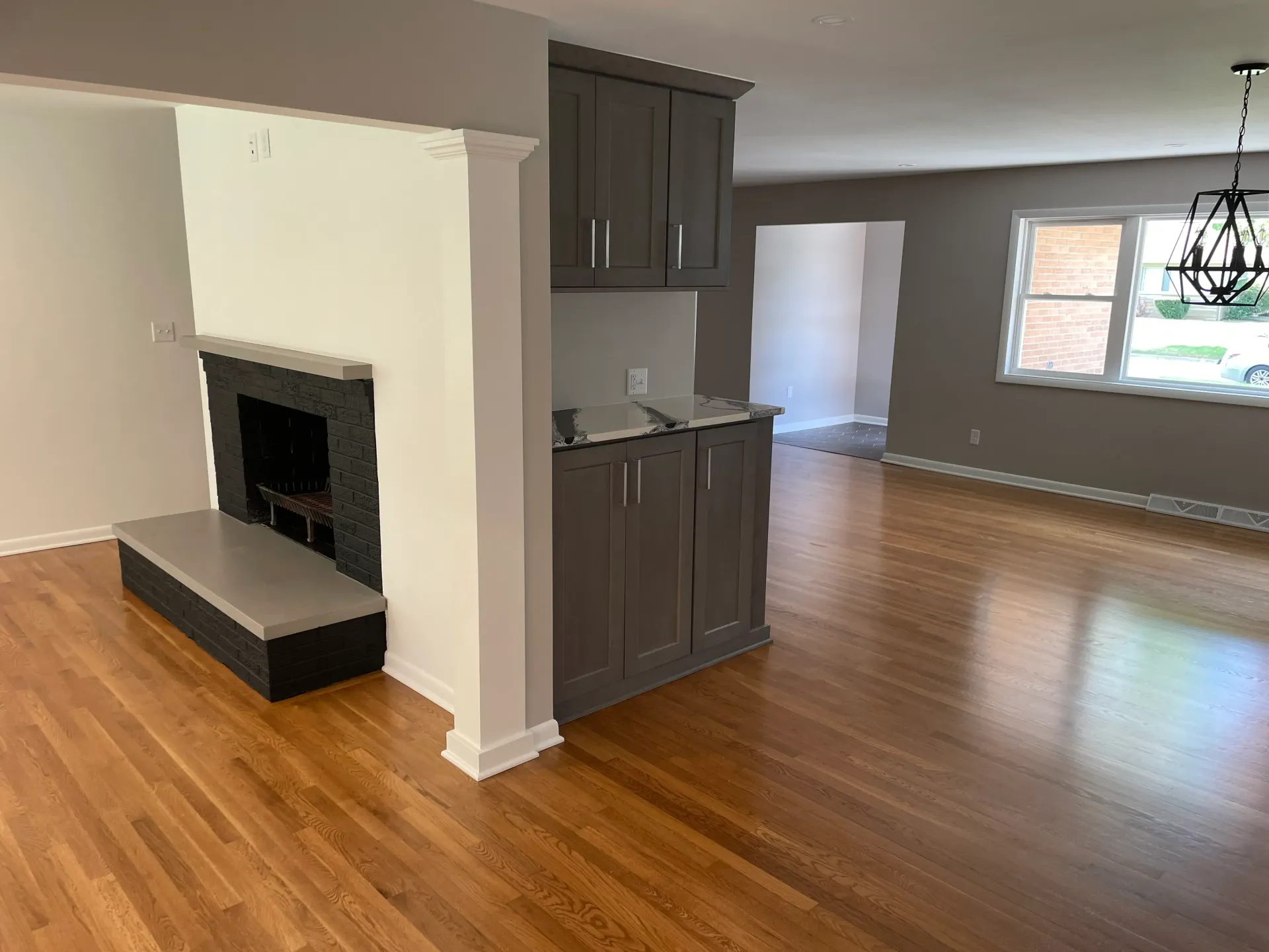Living room with hardwood floors, dark grey cabinets, fireplace, and chandelier.