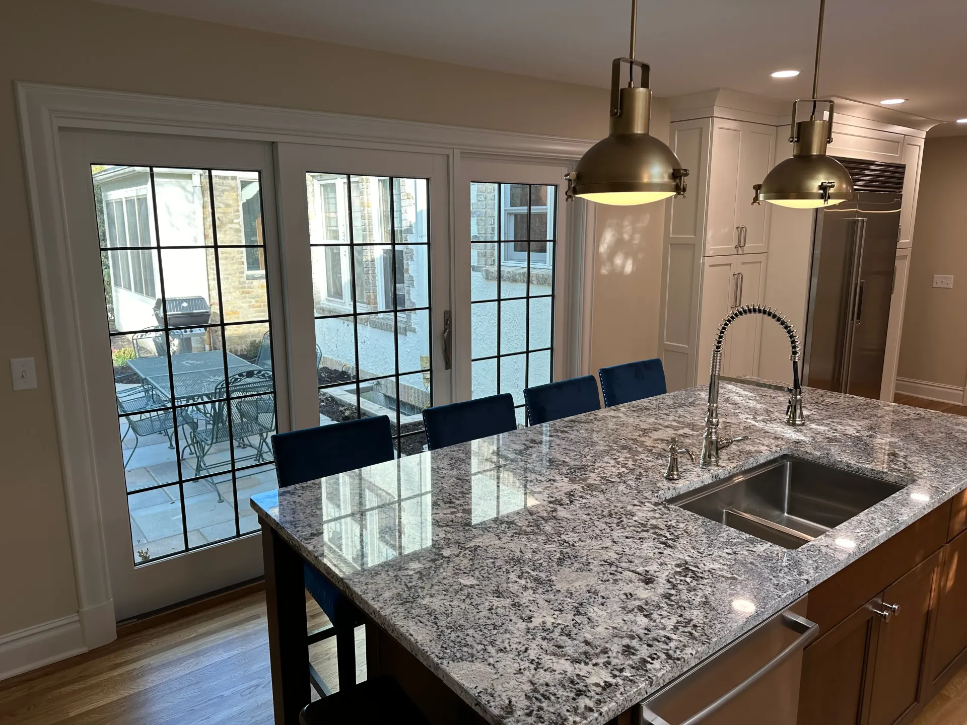 Kitchen with granite countertop island, sink, and pendant lights; French doors in background.