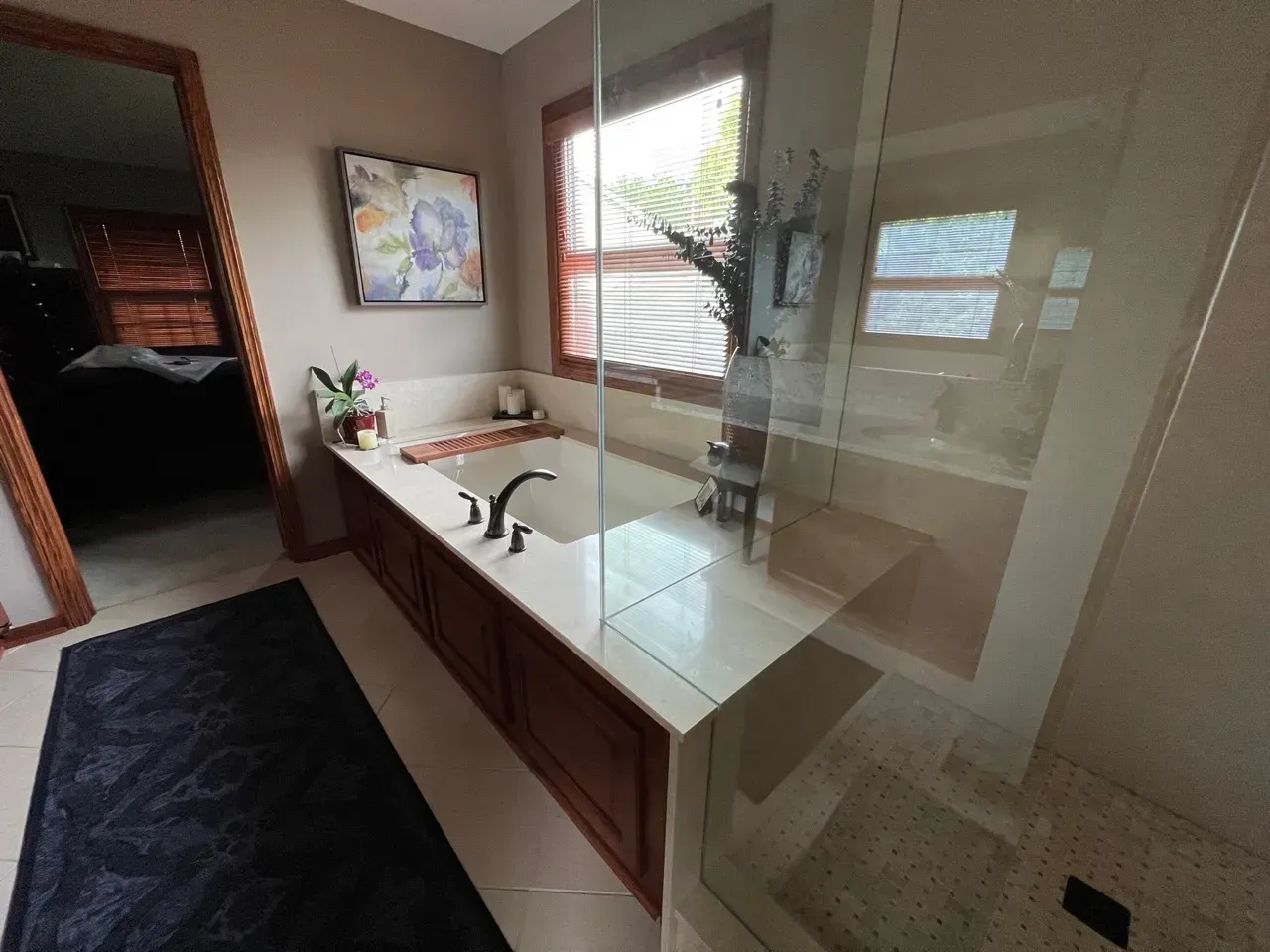 Bathroom with a soaking tub, shower, and window. Brown cabinets, white counter, glass shower.