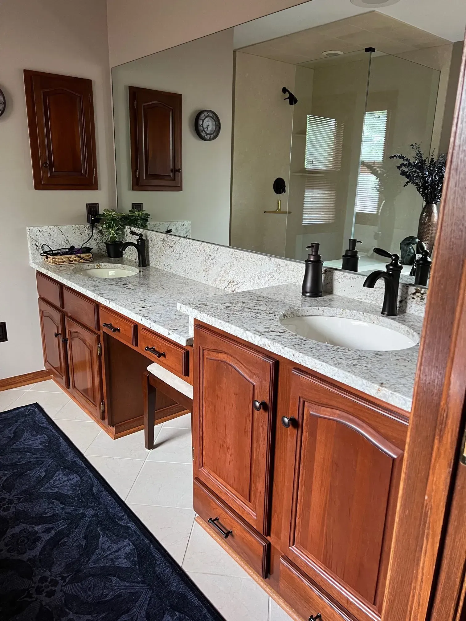 Bathroom with wood cabinets, white countertop, large mirror, and black fixtures.