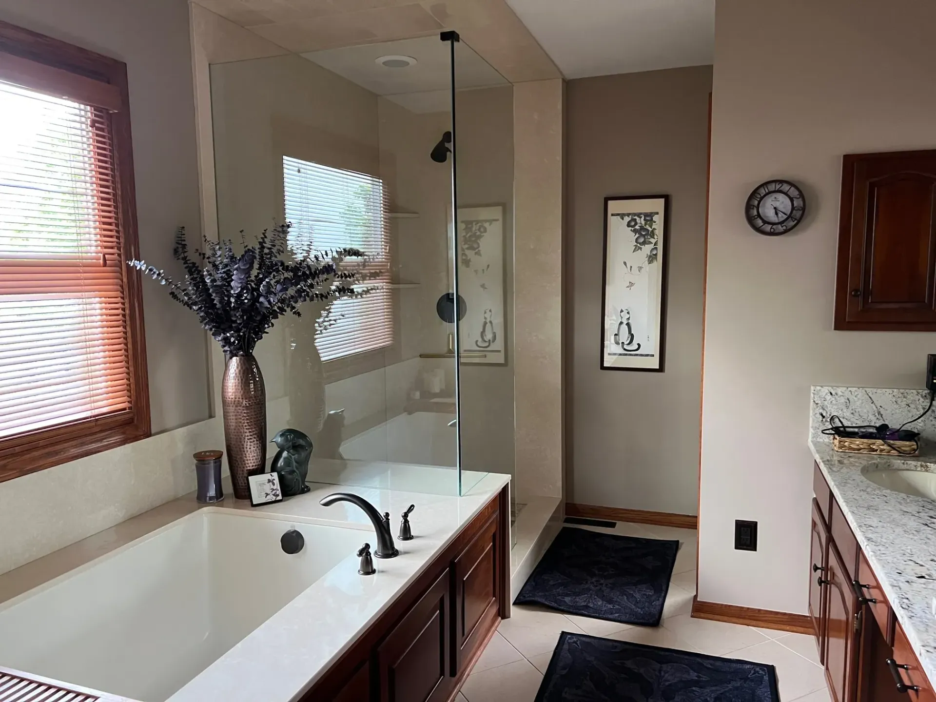 Bathroom with a bathtub, glass shower, wooden cabinets, beige walls, and lavender flowers in a vase.