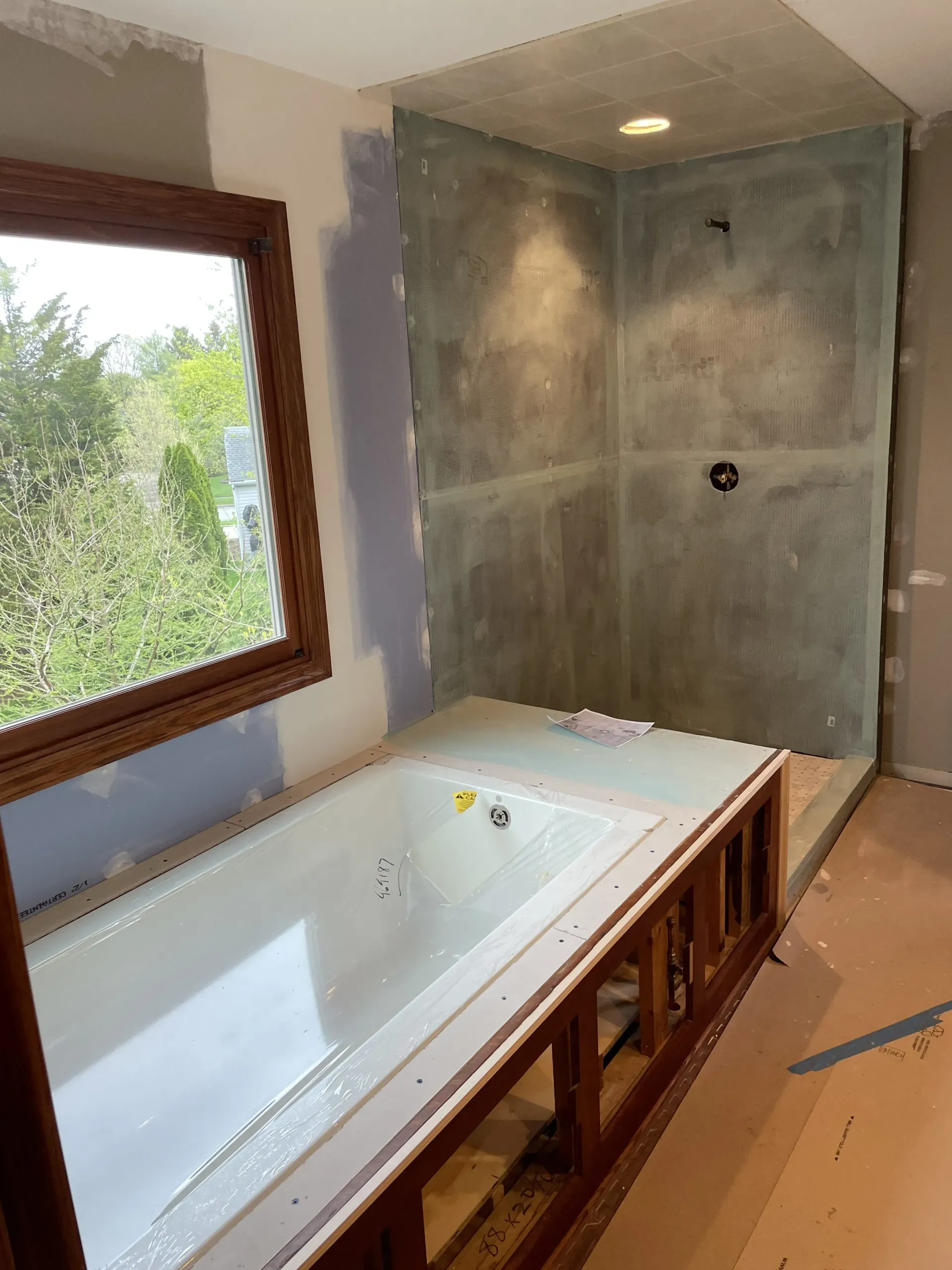 Bathroom under construction with a built-in tub and shower. The shower walls are gray, and a window is on the left.
