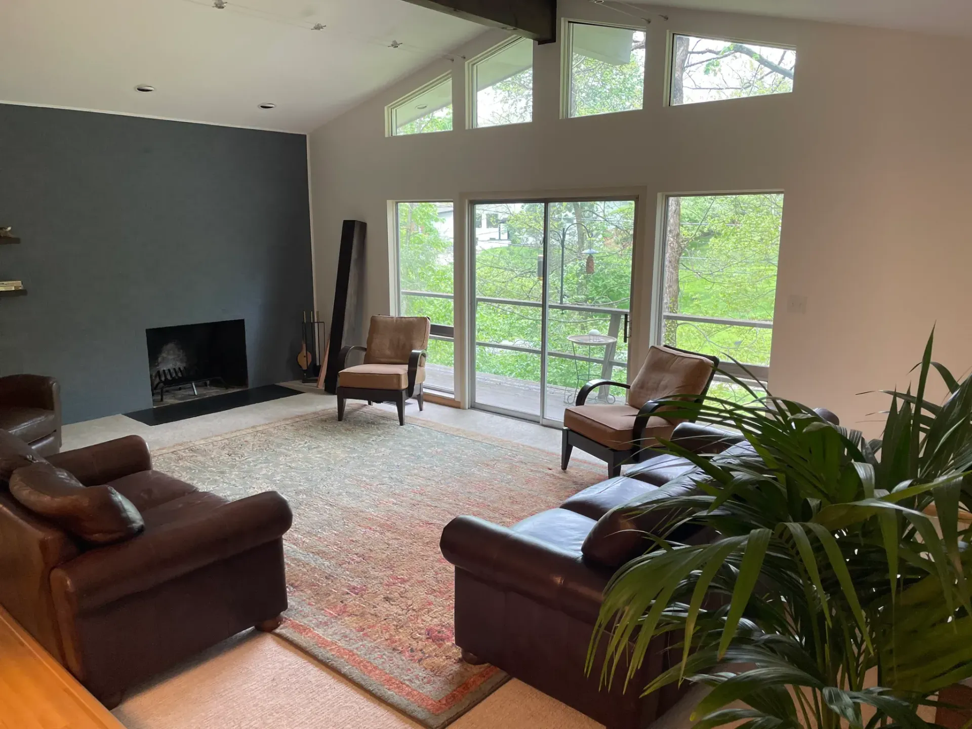 Living room with dark blue wall, fireplace, large windows overlooking trees, leather furniture.