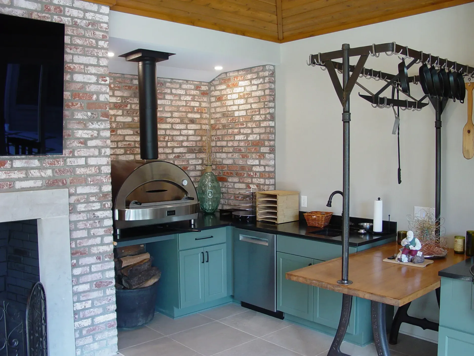 Outdoor kitchen with brick, teal cabinets, pizza oven, and butcher rack.
