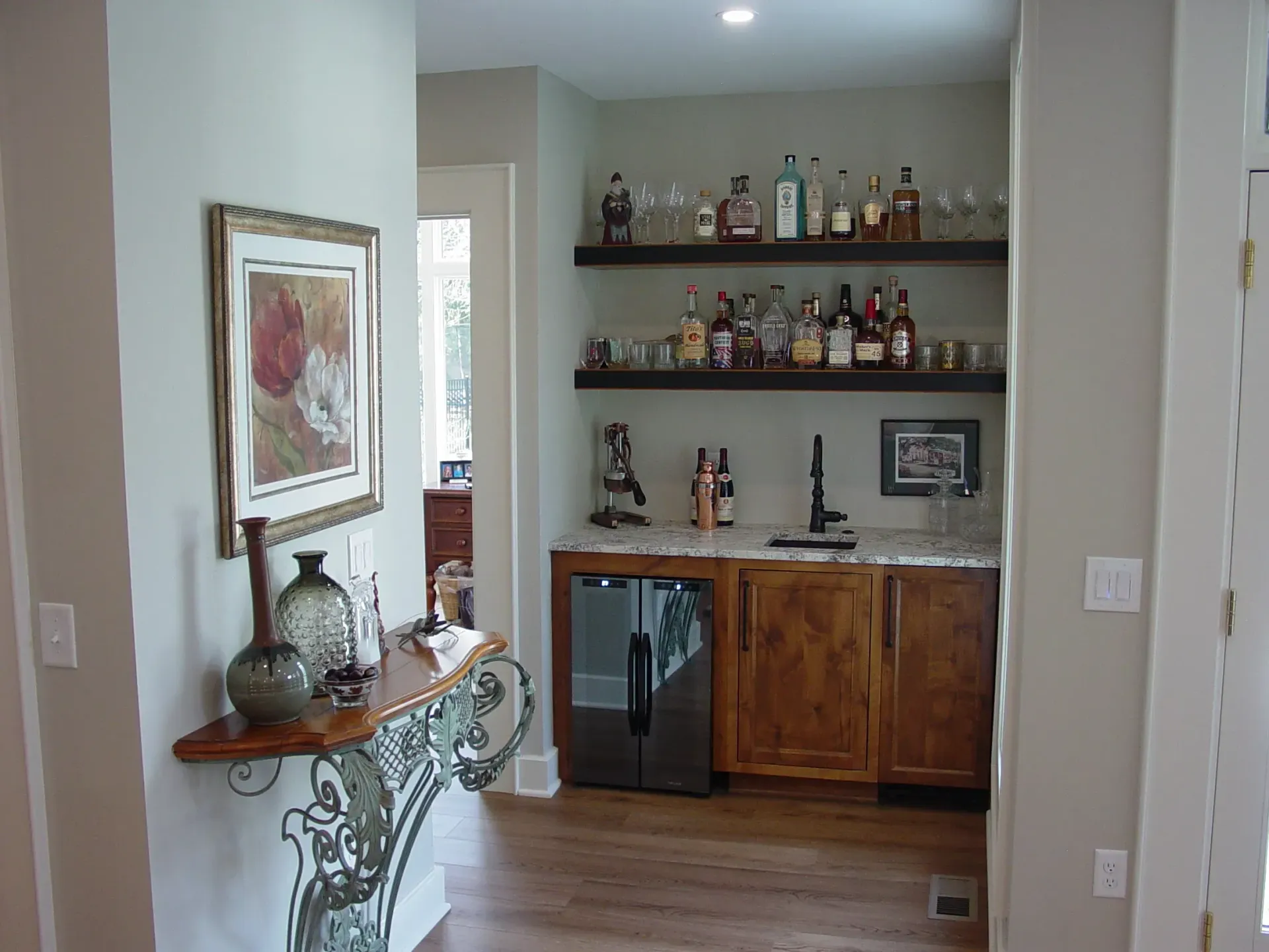 Home bar with liquor bottles on shelves, cabinets, and a small refrigerator.