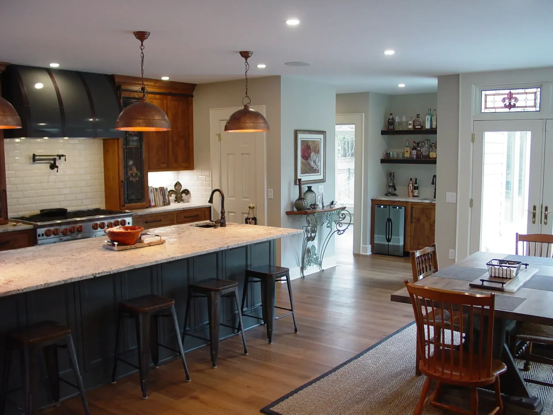 Spacious kitchen with dark island, copper pendants, and bar area. Dining table in foreground.