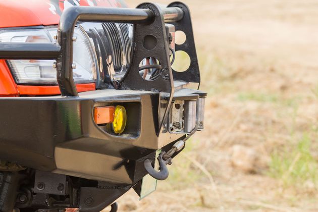 Orange off-road vehicle front bumper with winch and yellow fog light on a dirt road