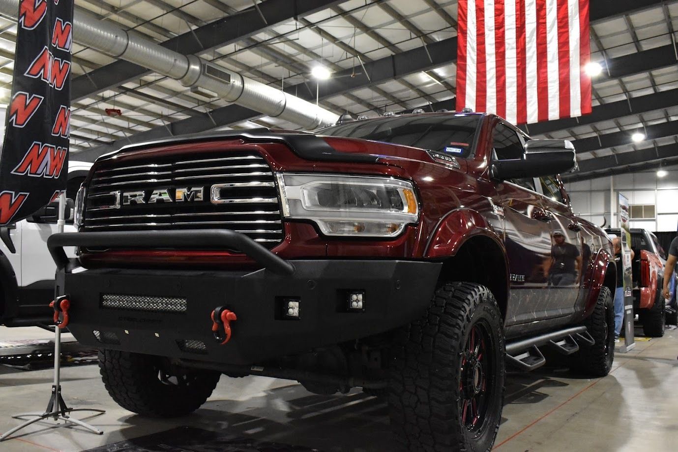 Lifted burgundy pickup truck on display in a warehouse with American flags overhead