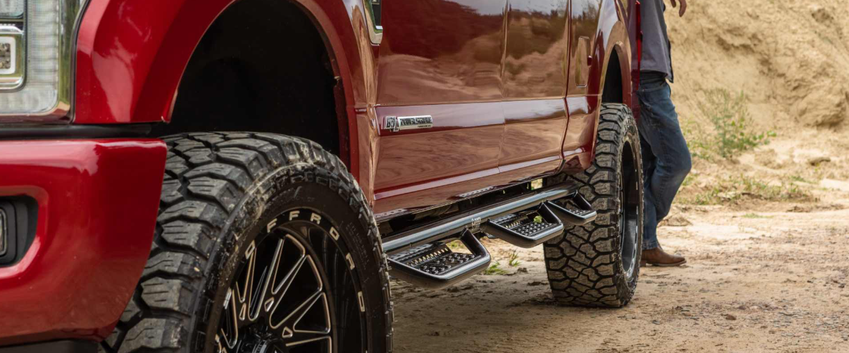 Red off-road truck with large tires on a dirt trail beside a person.