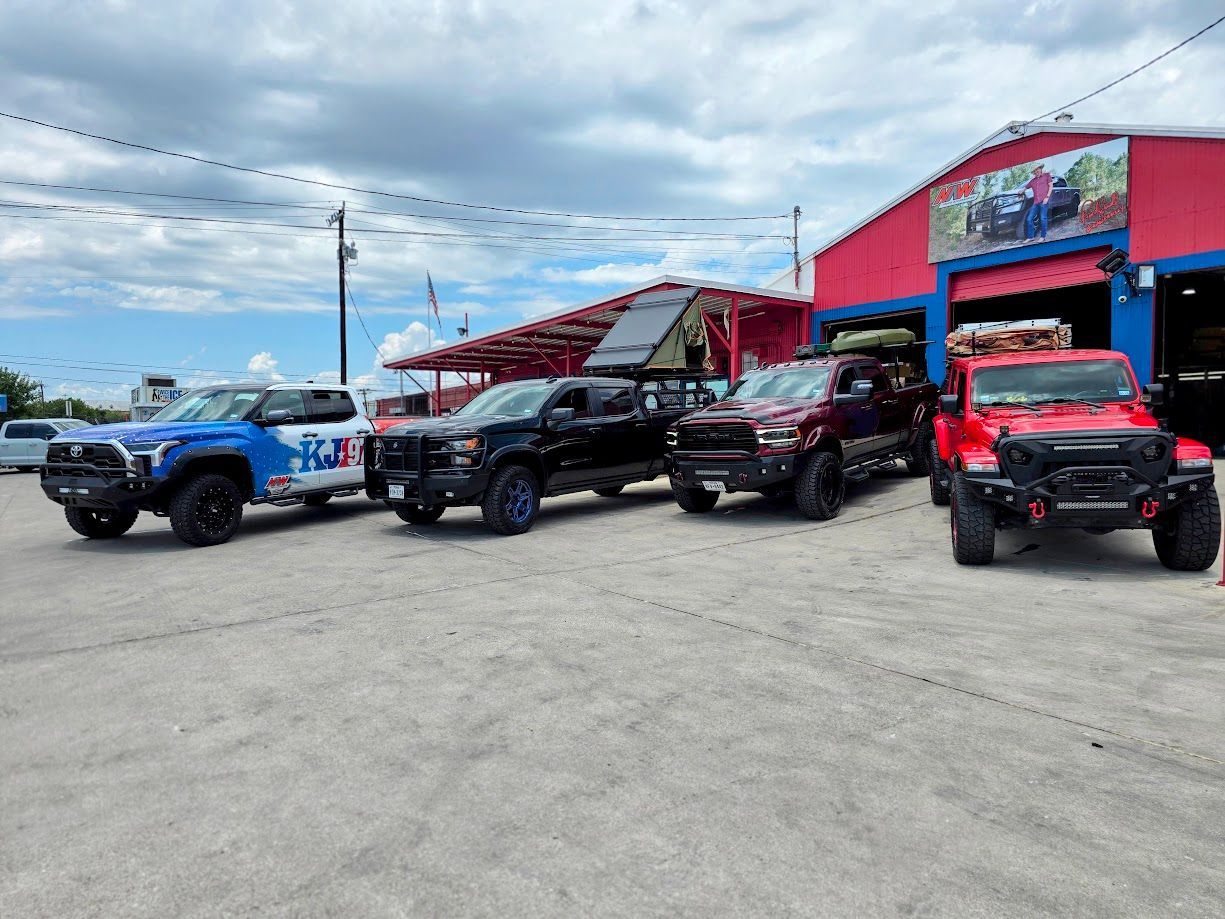 Four off-road vehicles parked outside a bright red dealership under a cloudy sky