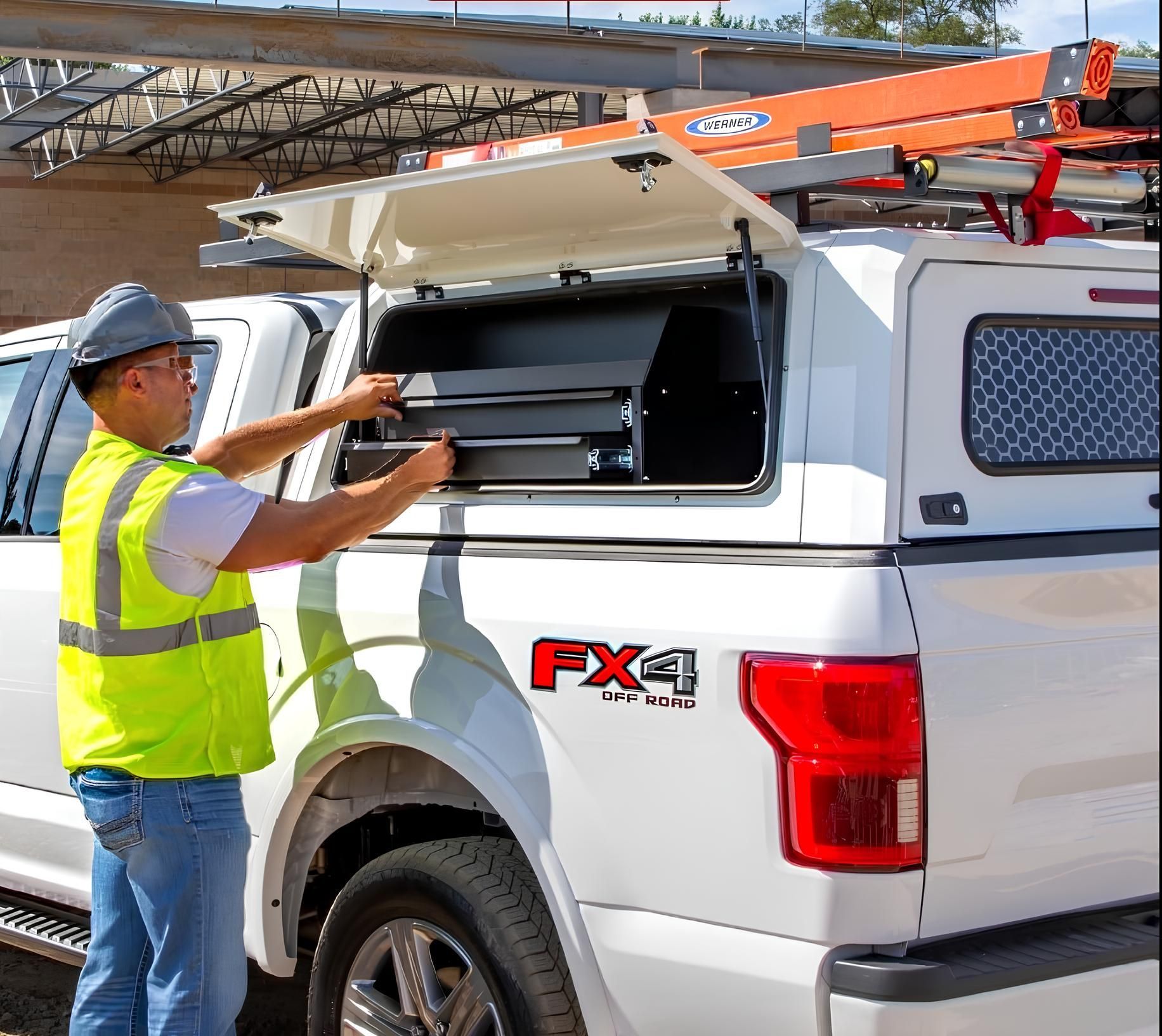 Worker loading tools into white utility truck with open side compartment and roof ladder rack