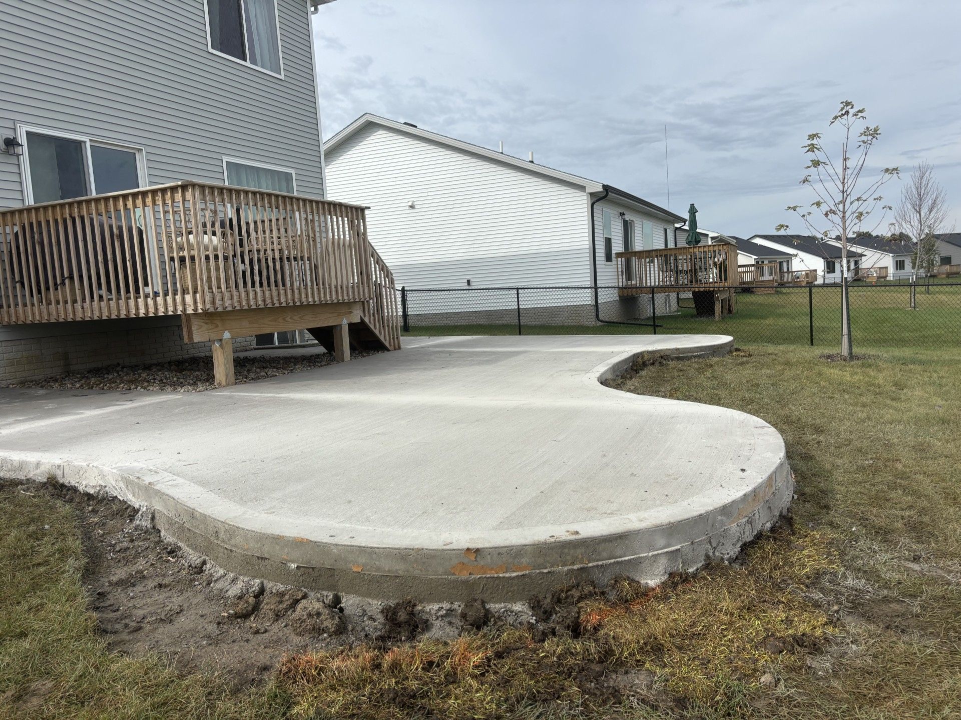 Concrete patio beside a wooden deck and a grassy yard. Cloudy sky in the background.