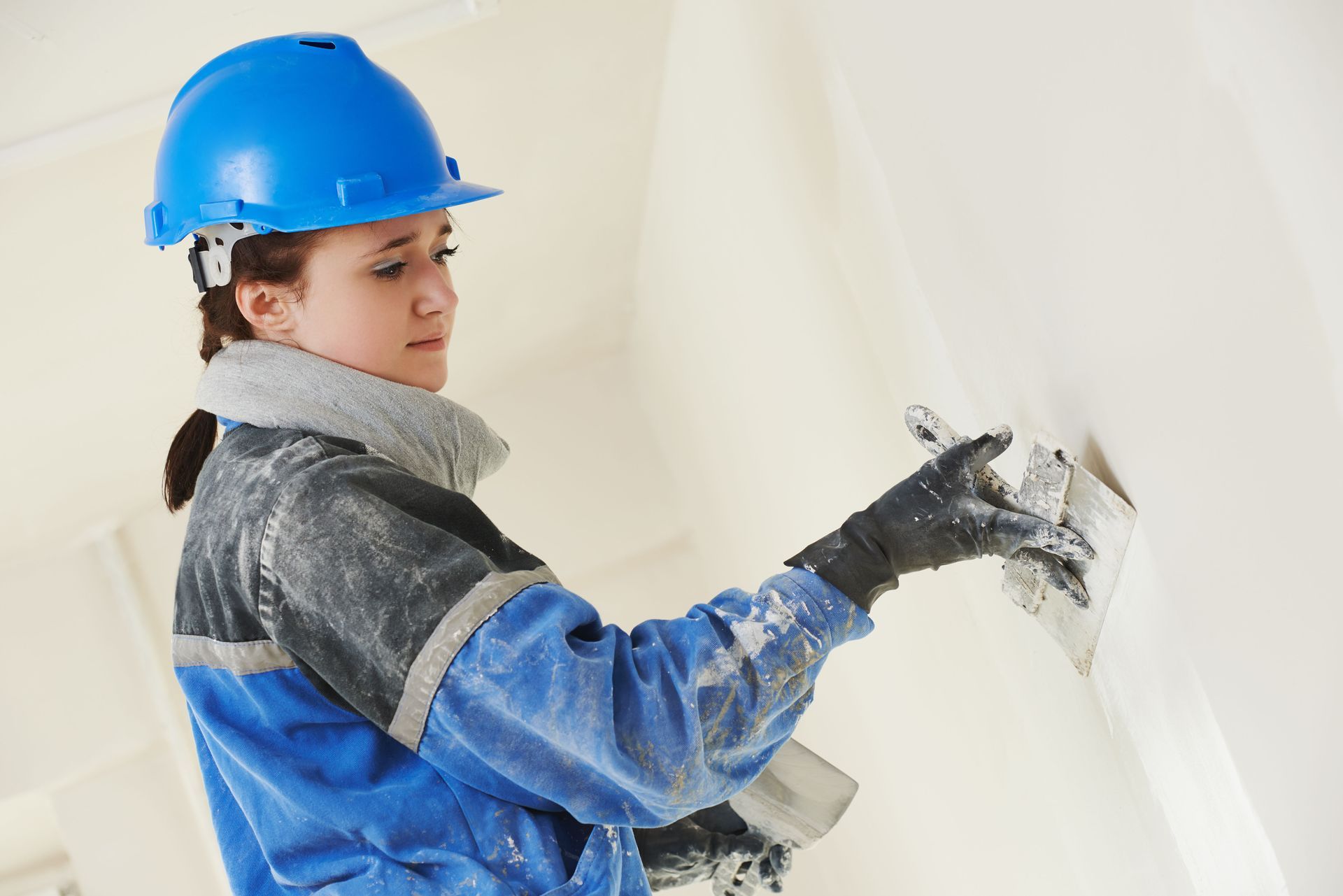 Worker applying gray stucco to a wall with a trowel on an extension pole