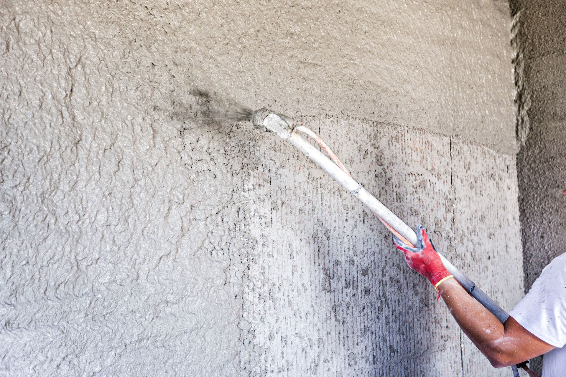 Worker applying gray stucco to a wall with a trowel on an extension pole
