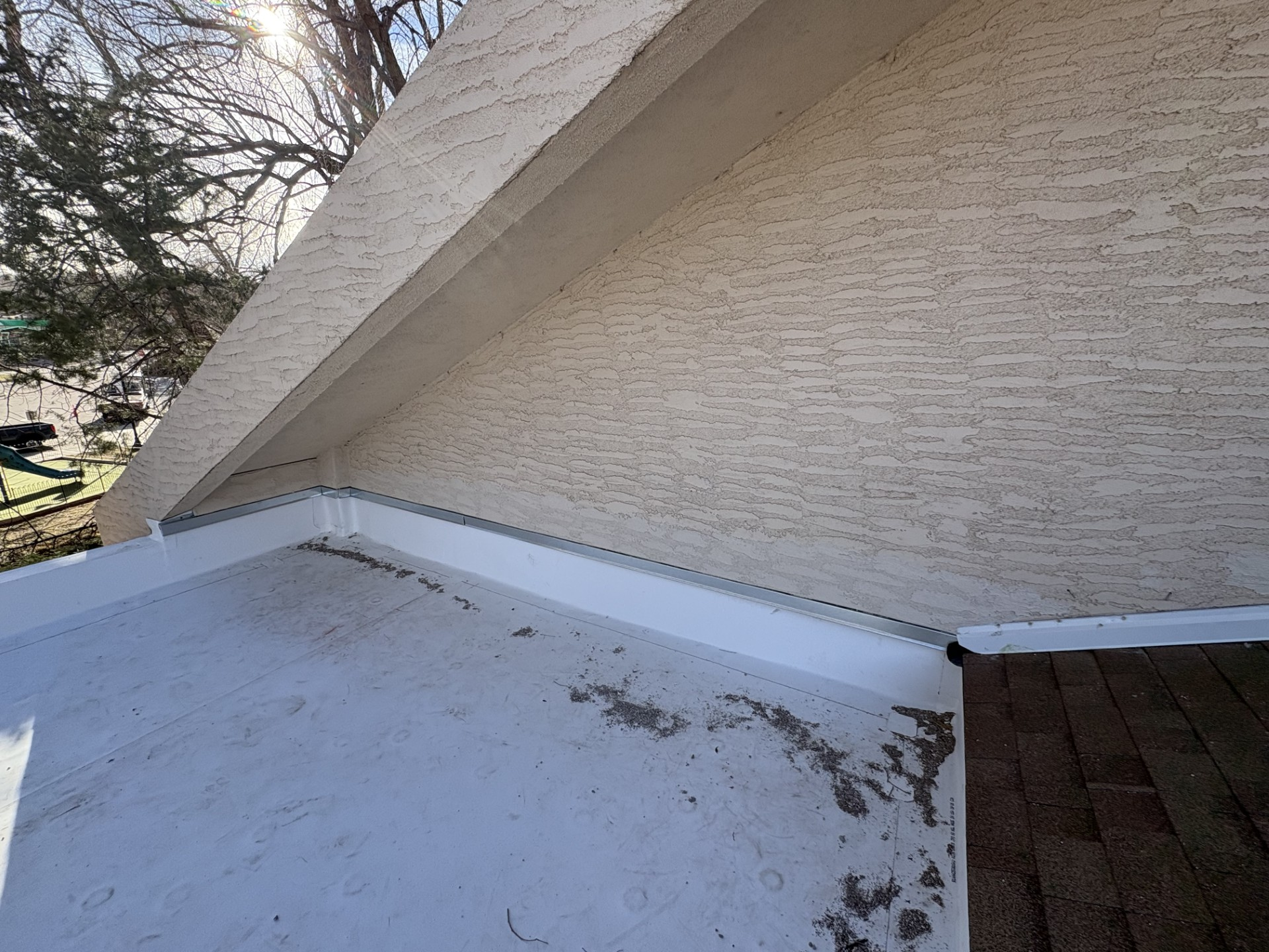 View of a white flat roof section with textured wall above; part of a brick roof is also visible.