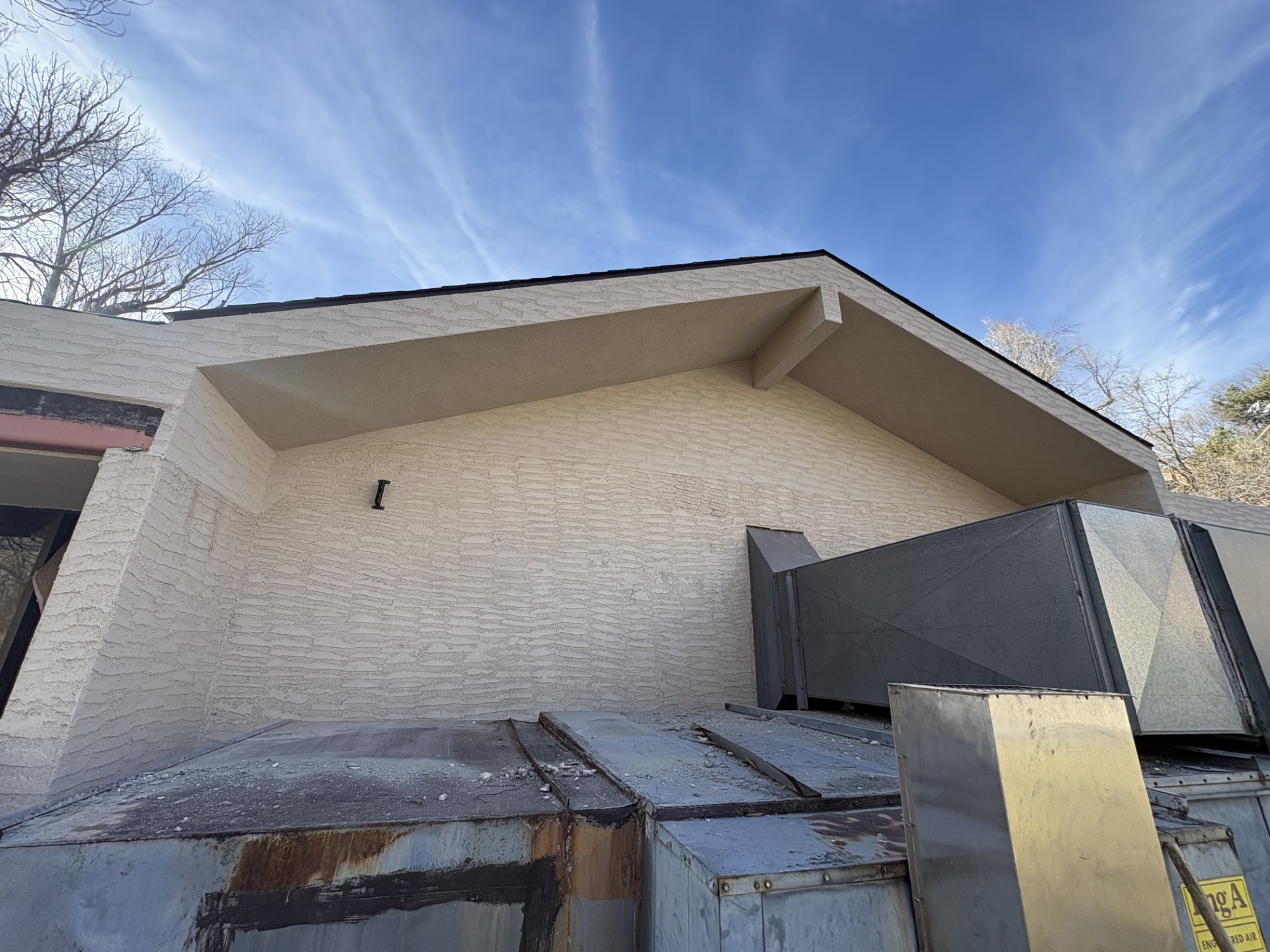 Tan stucco building exterior with angled roofline; metal ventilation equipment on a flat roof.