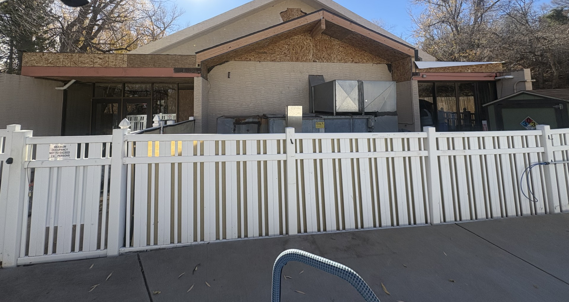 White fence in front of a building with a beige stucco exterior and a brown roof.