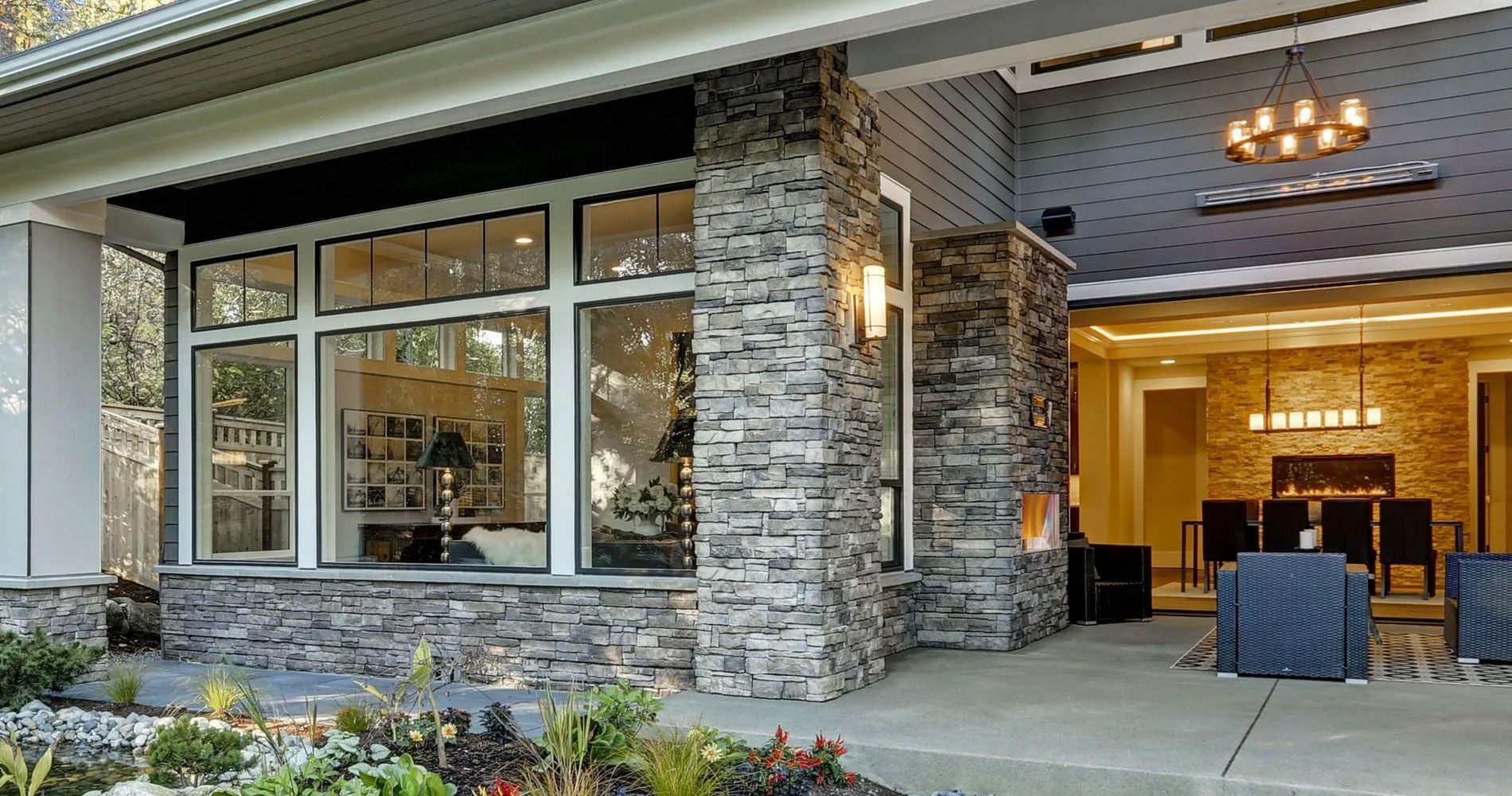 Exterior view of a modern home with stone accents, large windows, and a covered patio with chairs.