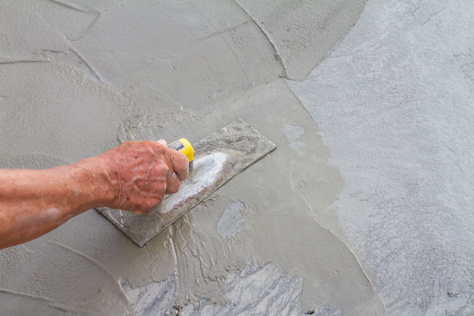 Hand using a trowel to apply wet cement to a wall.