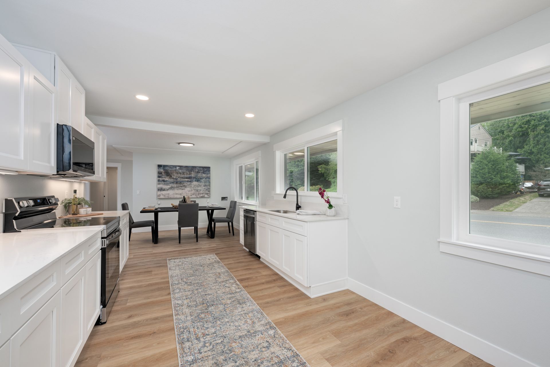 Bright, modern kitchen with white cabinets, countertops, and appliances. Dining area in the background.
