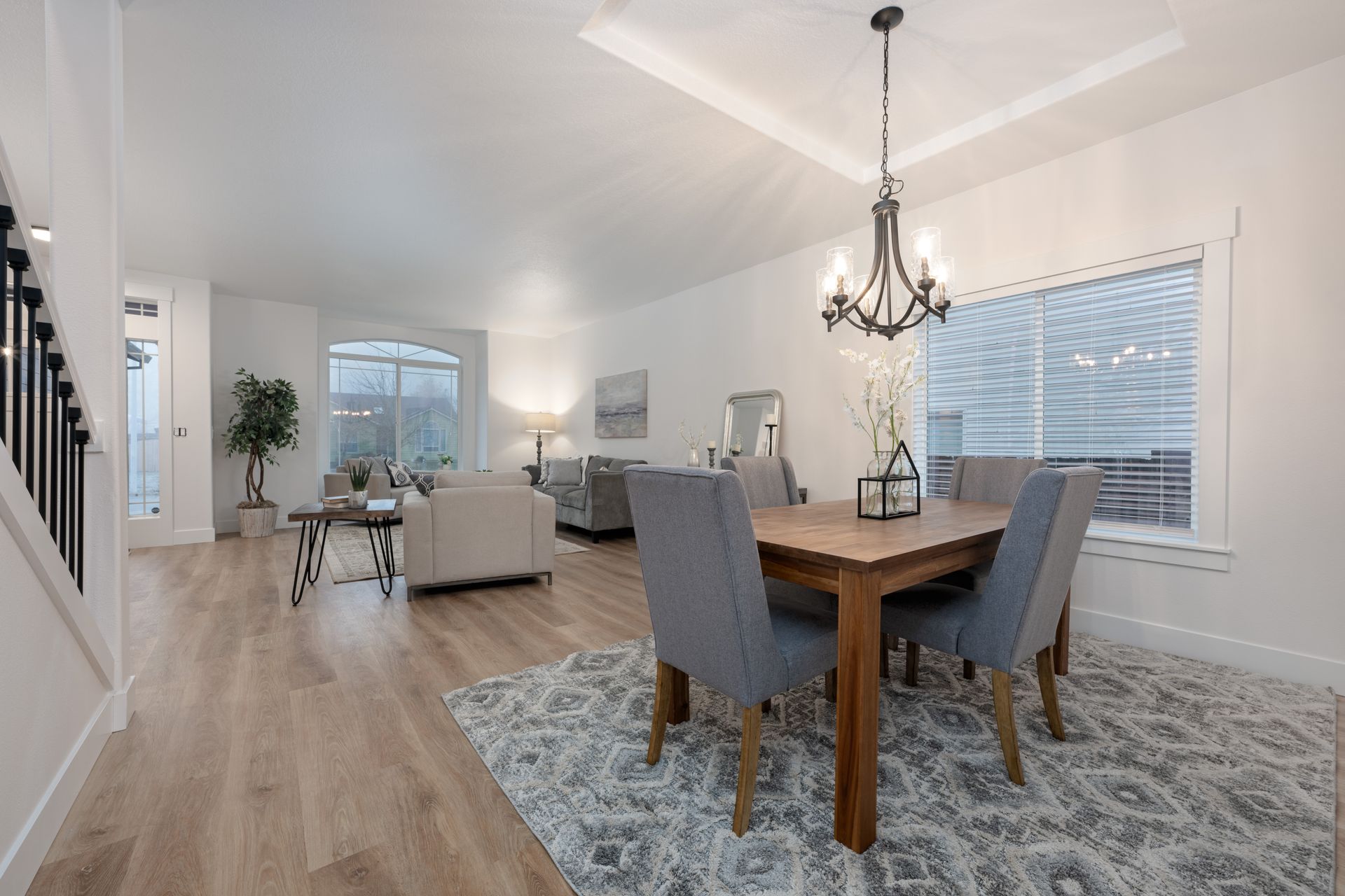 Open-concept dining and living area with light wood floors, gray chairs, and a chandelier.