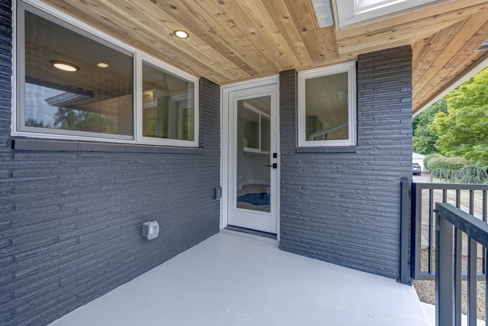 Covered porch with gray brick walls, a white door, and light wood ceiling.