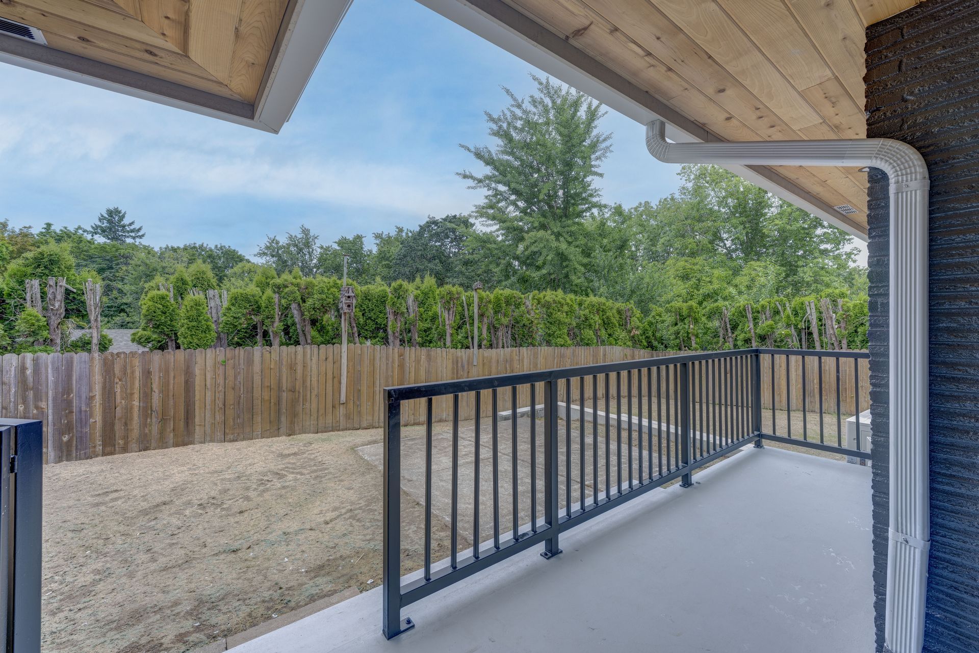 Balcony overlooking a backyard with a wooden fence and green trees.