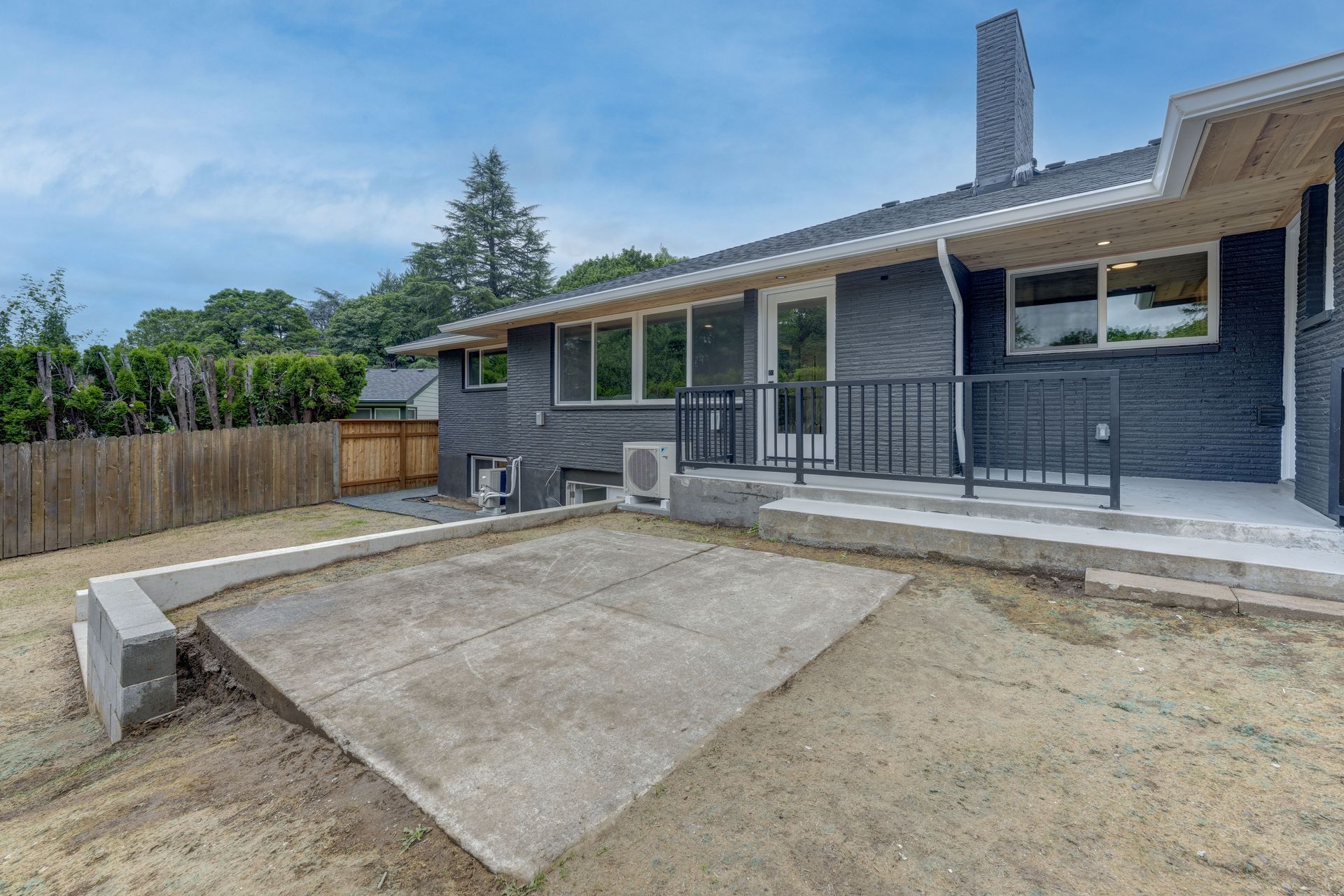 Backyard with concrete patio, gray house, brown fence, and overcast sky.