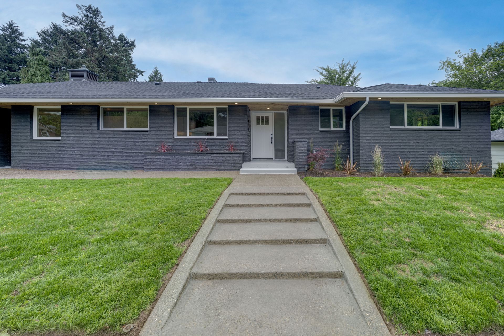 Gray house with concrete walkway, green lawn, and blue sky.