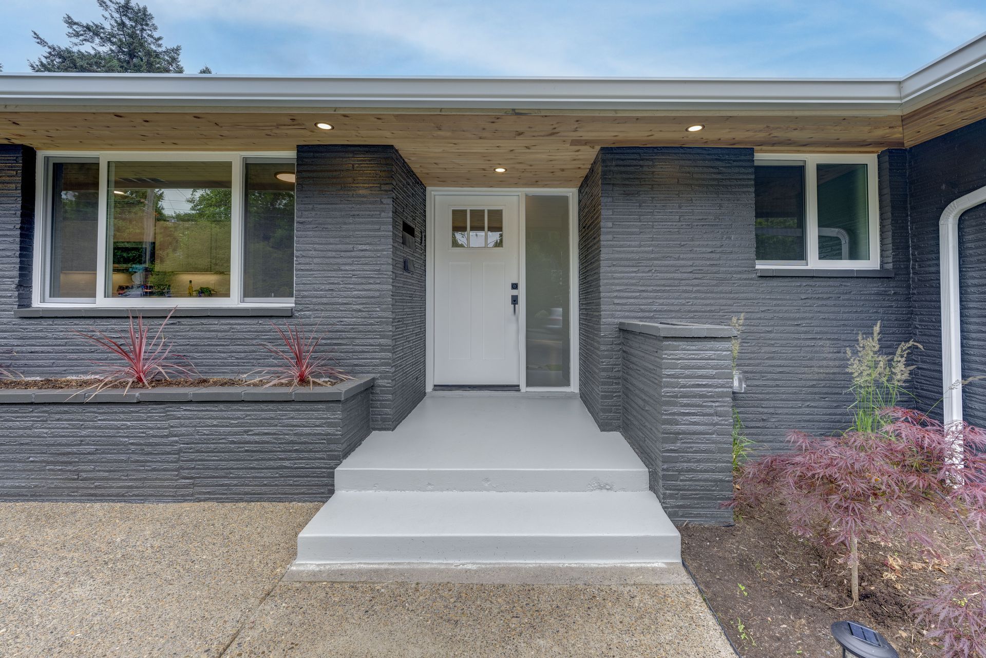 Front exterior of a house with a white door, grey steps, and black brick siding.