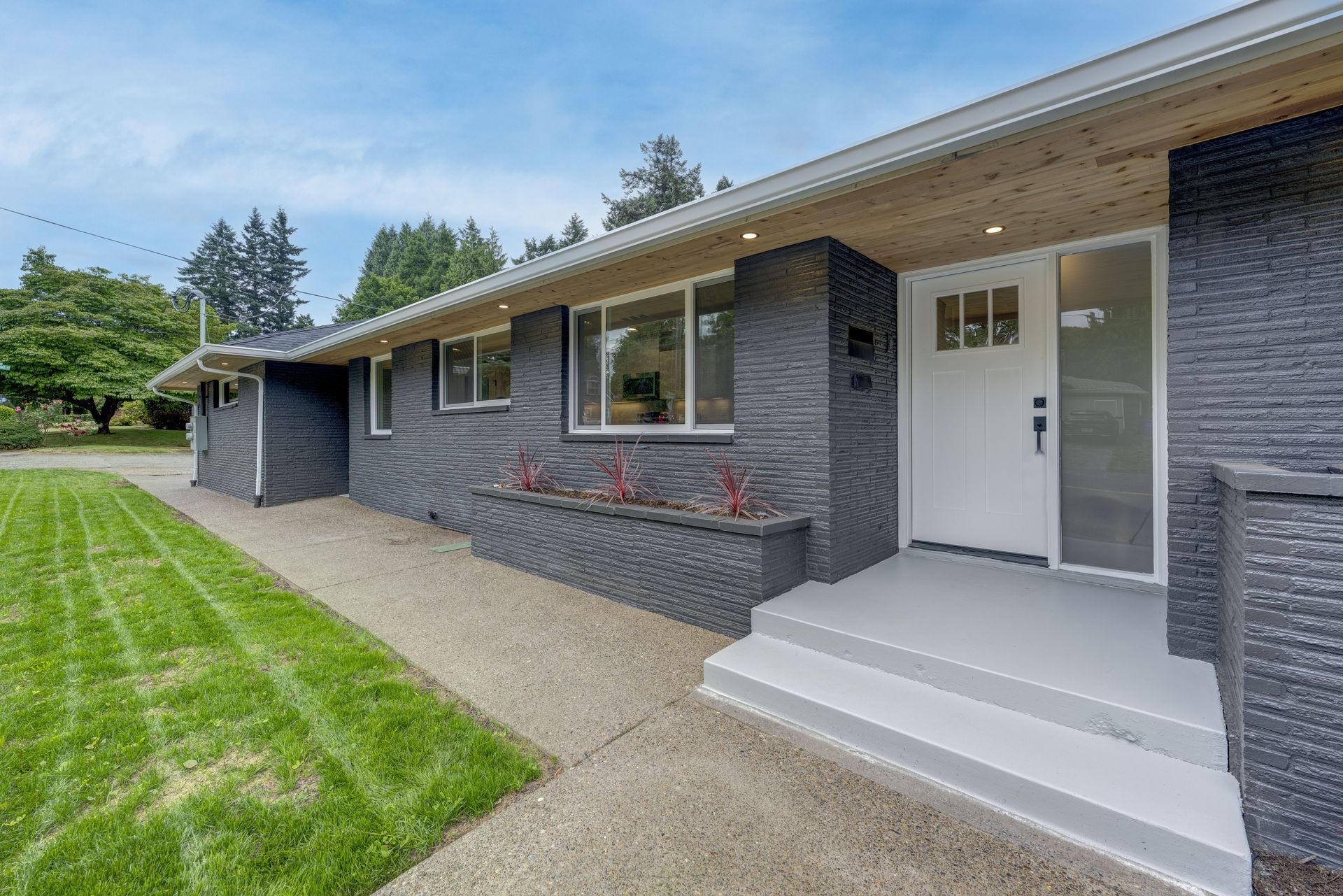 Black brick house with white door, steps, and trim; green lawn.