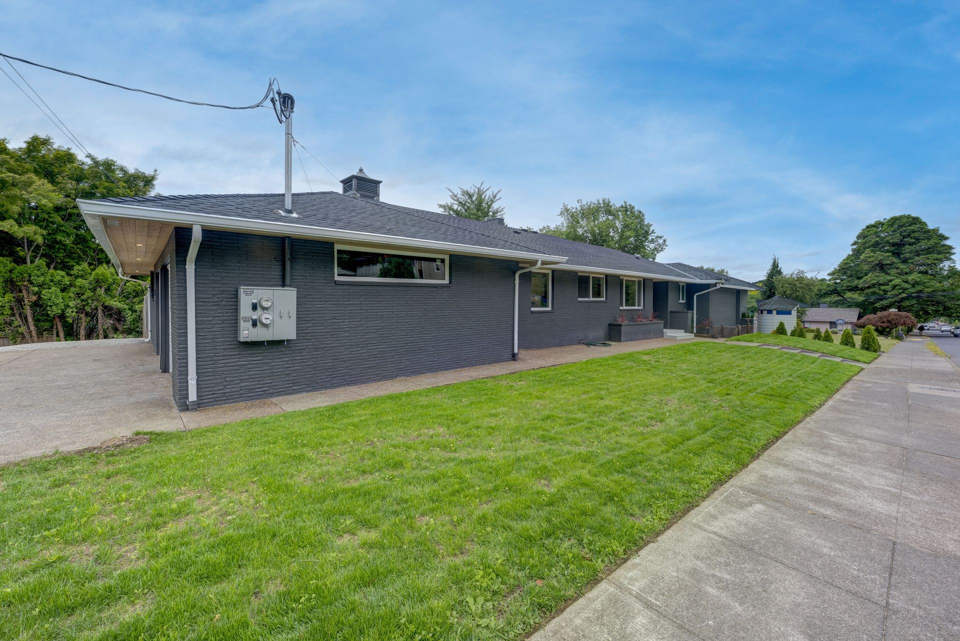 Gray ranch-style house with a green lawn and driveway under a blue sky.