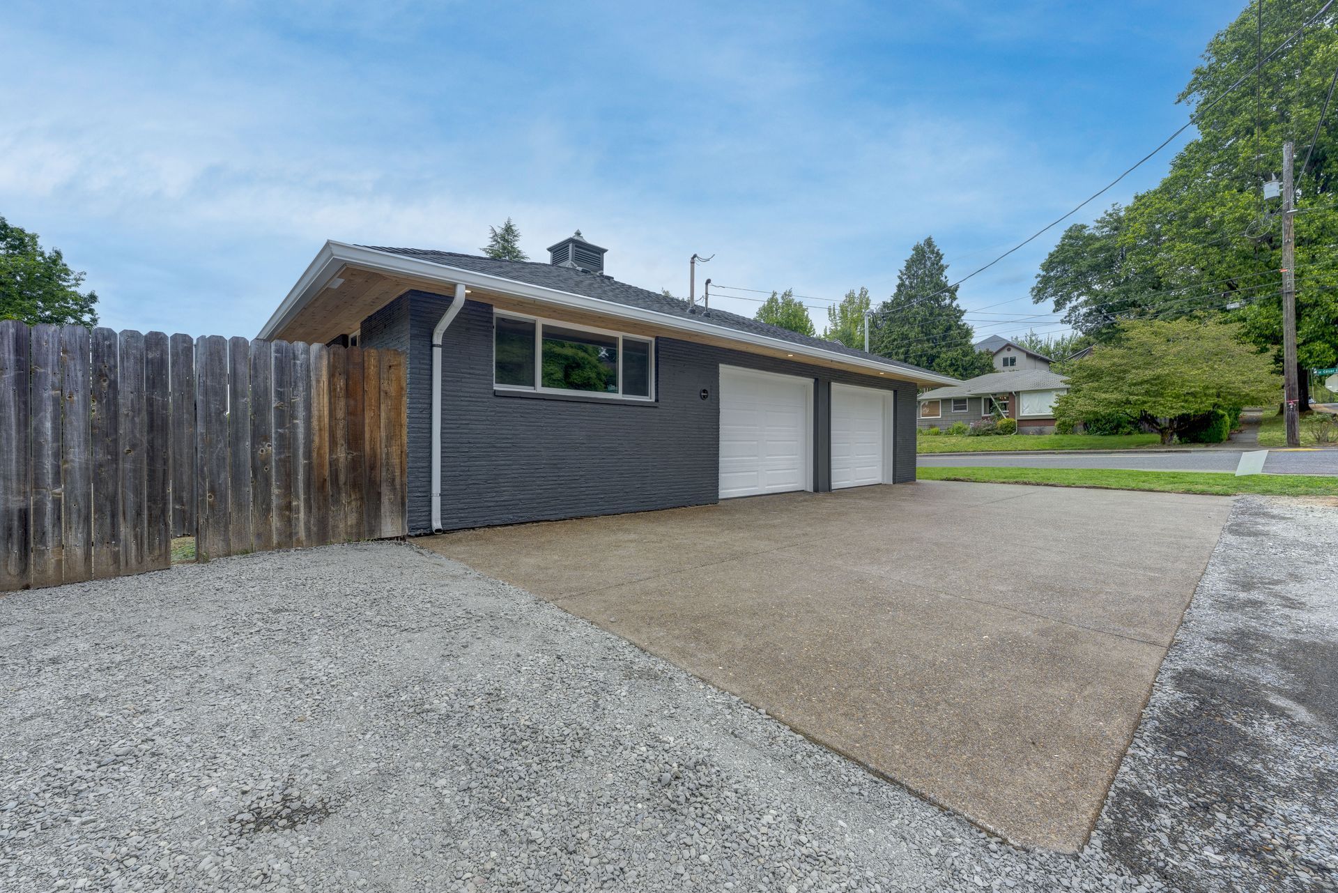 Gray garage with two white doors and a gravel driveway.