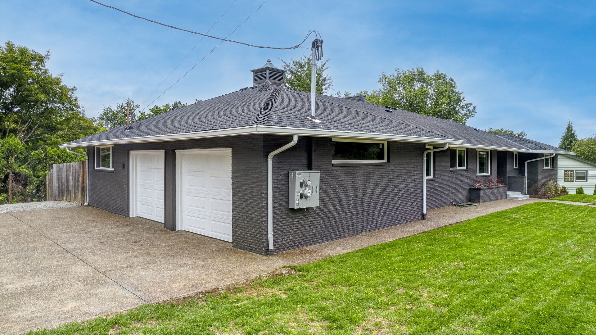 Black brick house with two-car garage, white doors, and green lawn.