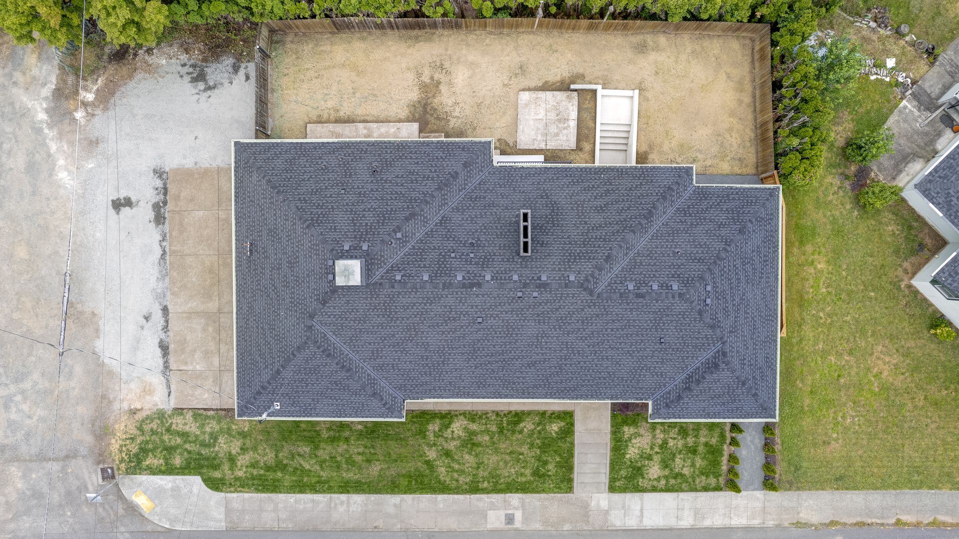 Aerial view of a house with a dark roof, surrounded by a yard and driveway.