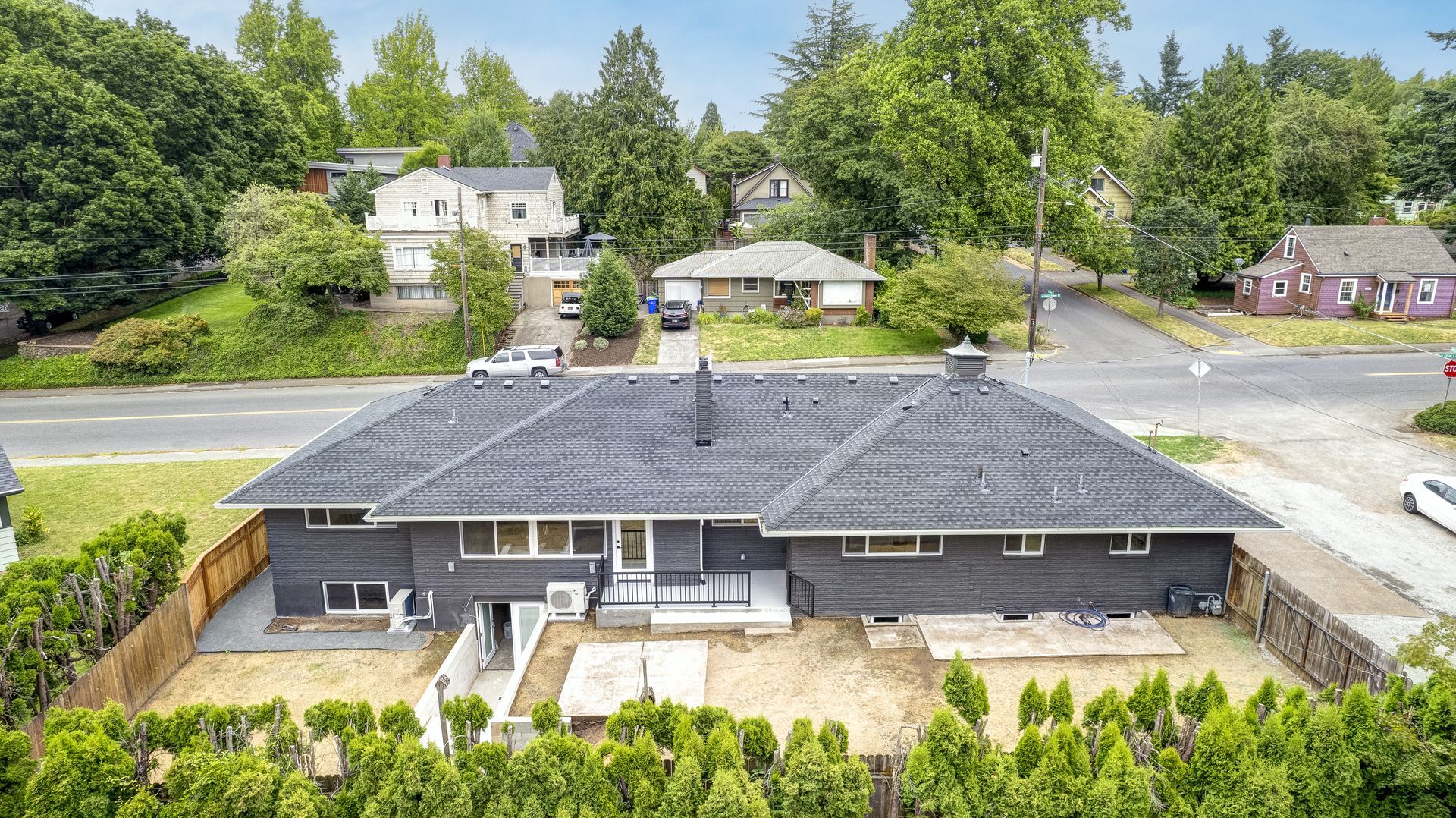 Aerial view of a dark gray house with a large roof, surrounded by trees and other houses.