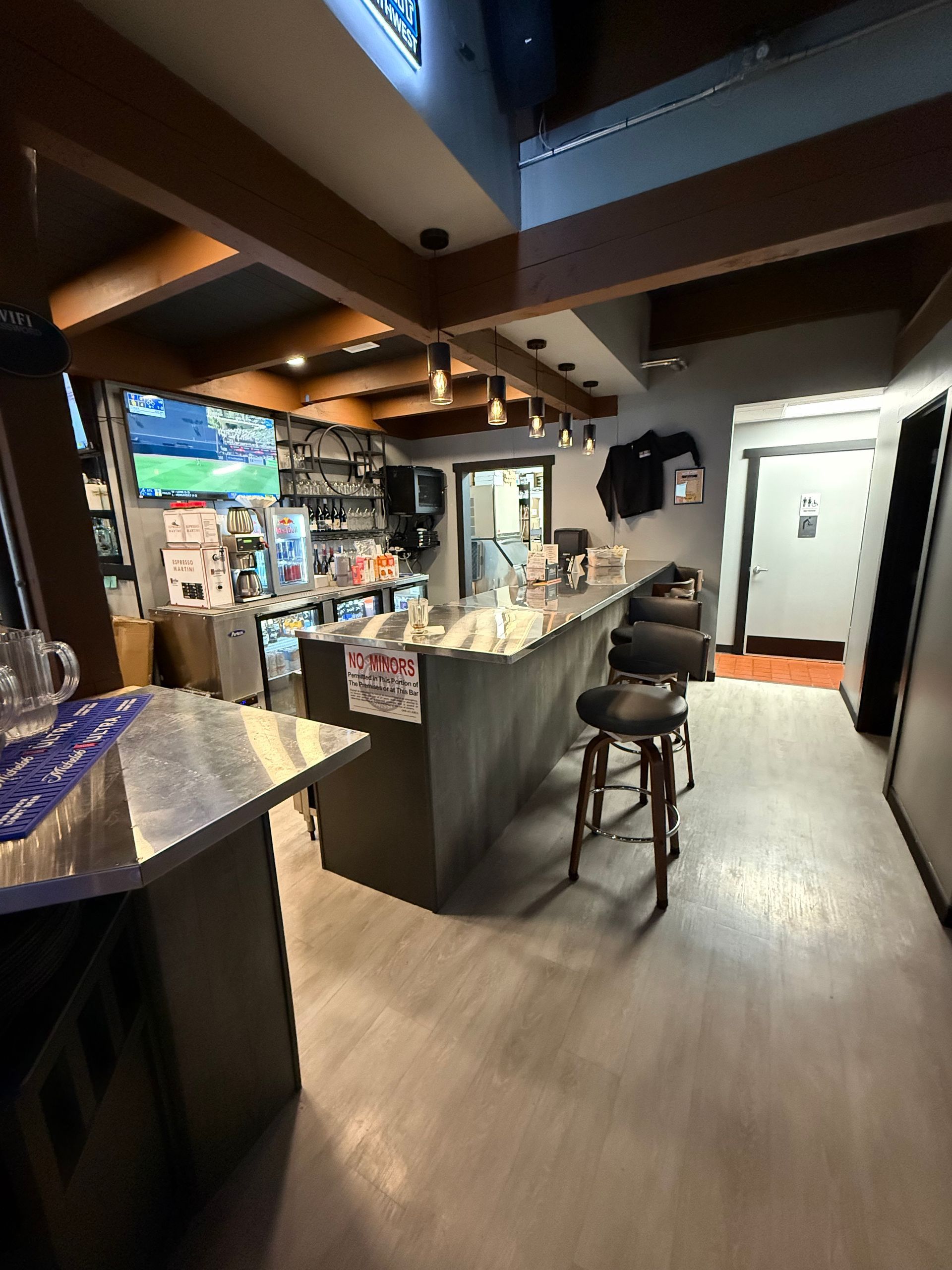 Bar interior with a gray bar, stools, TVs, and wooden beams.