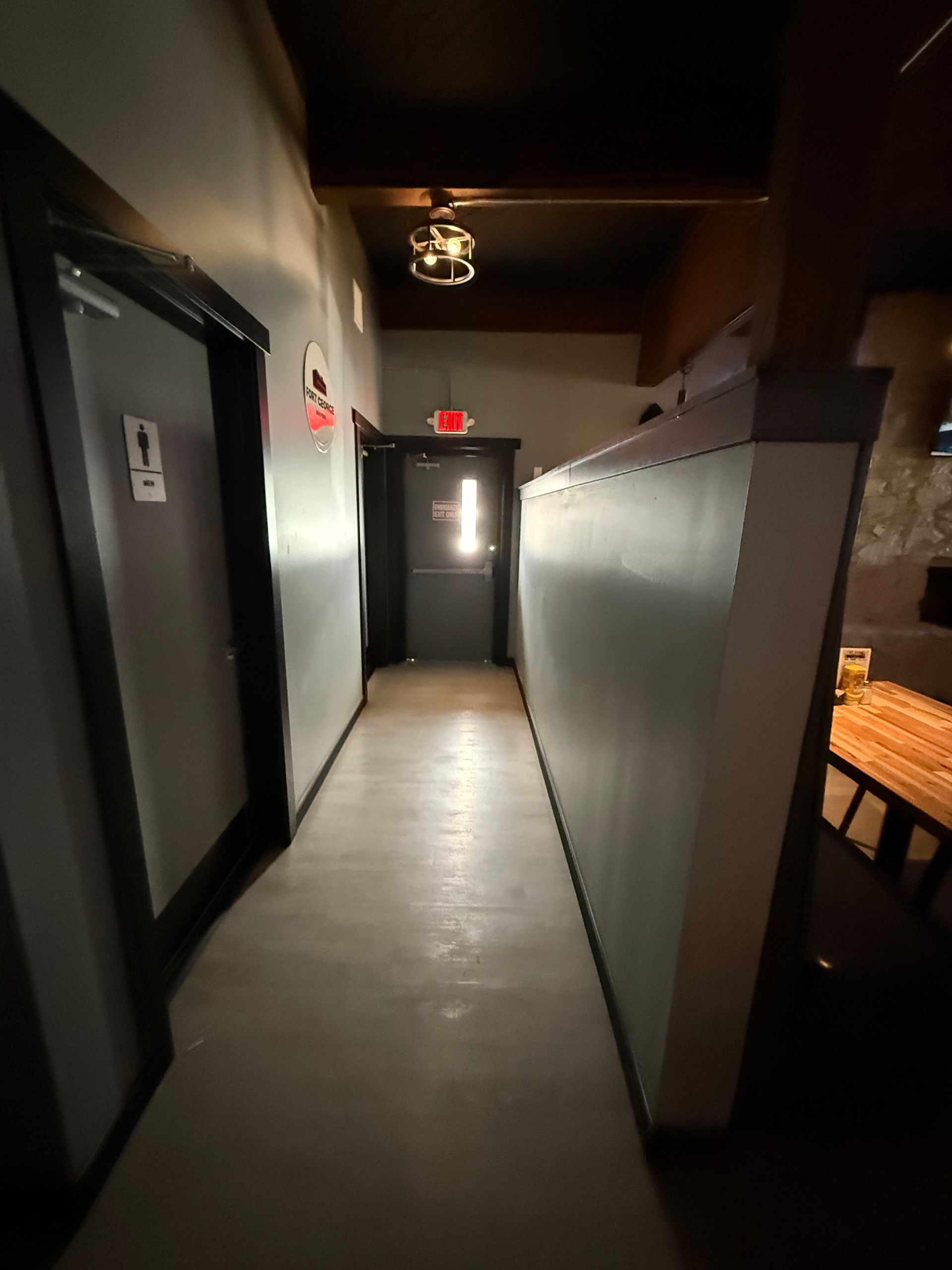 Narrow hallway with restroom door on left, exit door at the end, and white divider on right.