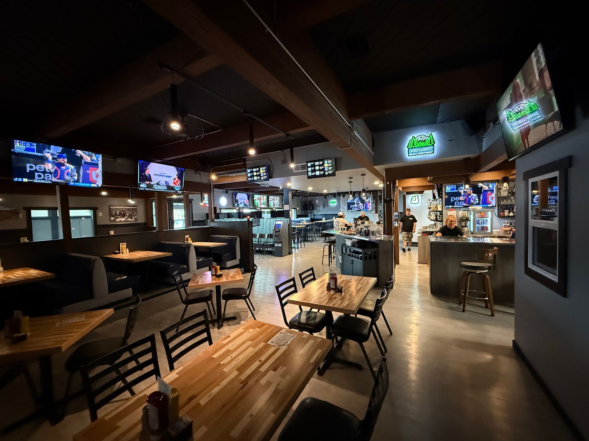 Interior of a bar with tables, booths, TVs showing sports, and a well-lit bar area.