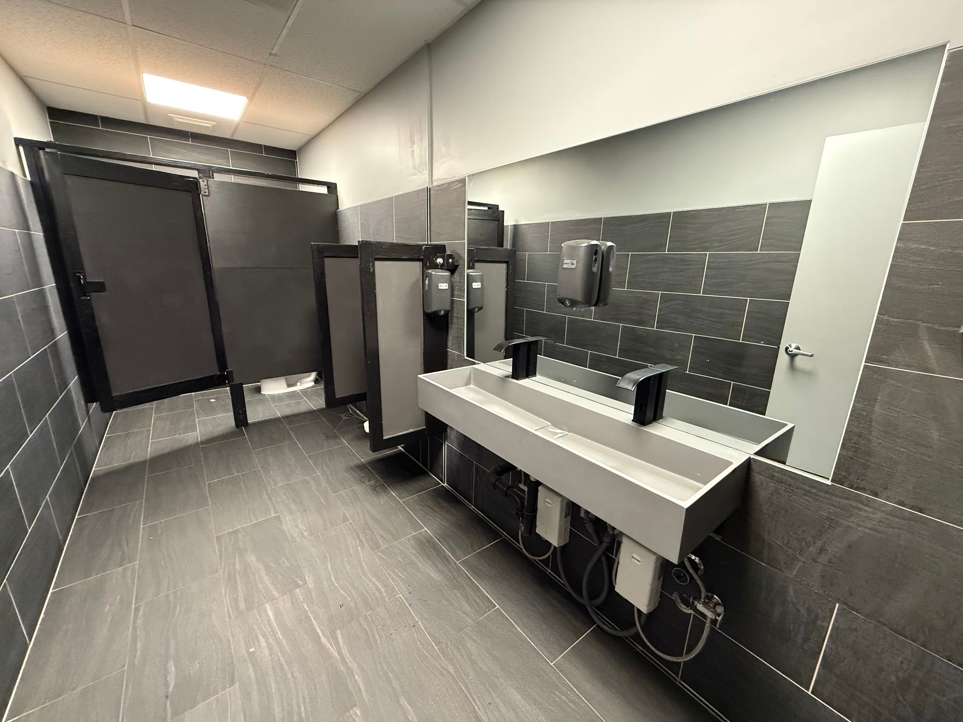 Modern public restroom with dark gray tile, sinks, and stalls.