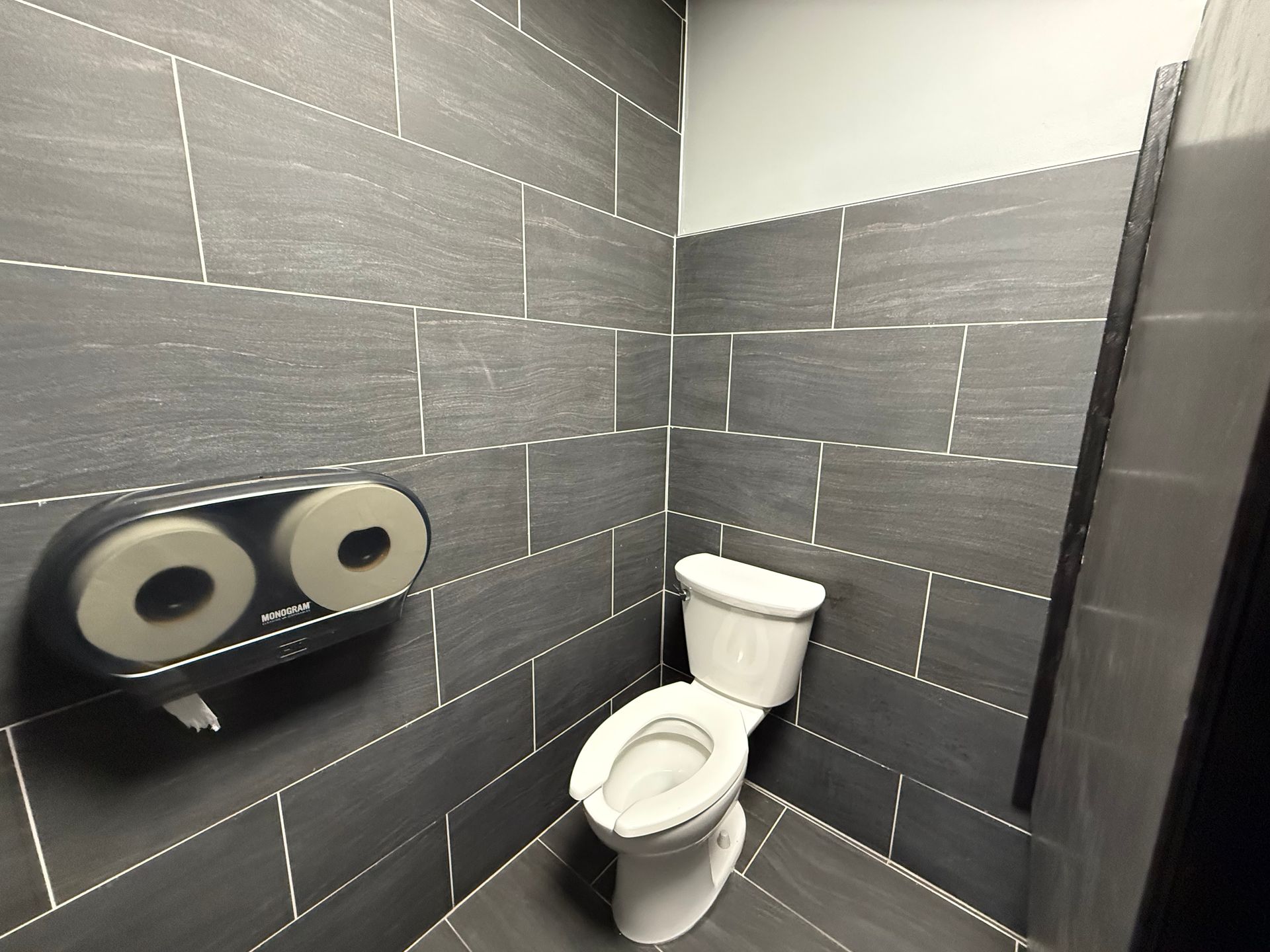 Gray-tiled restroom with a toilet, double toilet paper dispenser, and gray walls.