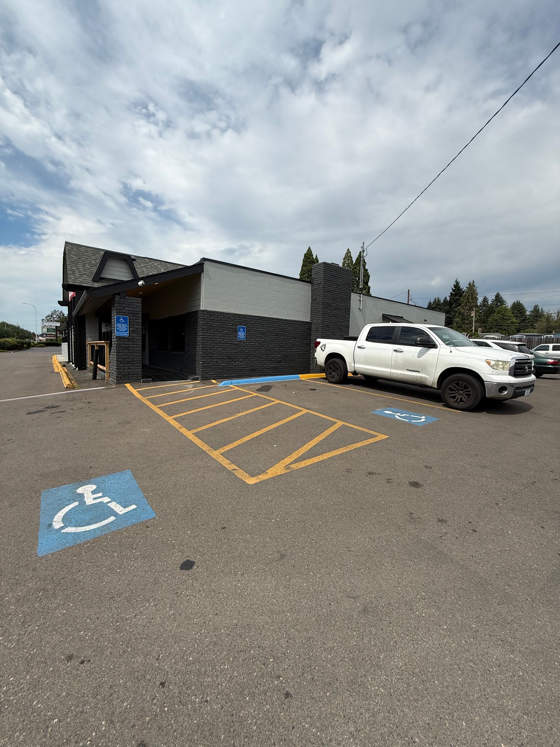 Building exterior with accessible parking space, white truck, and cloudy sky.