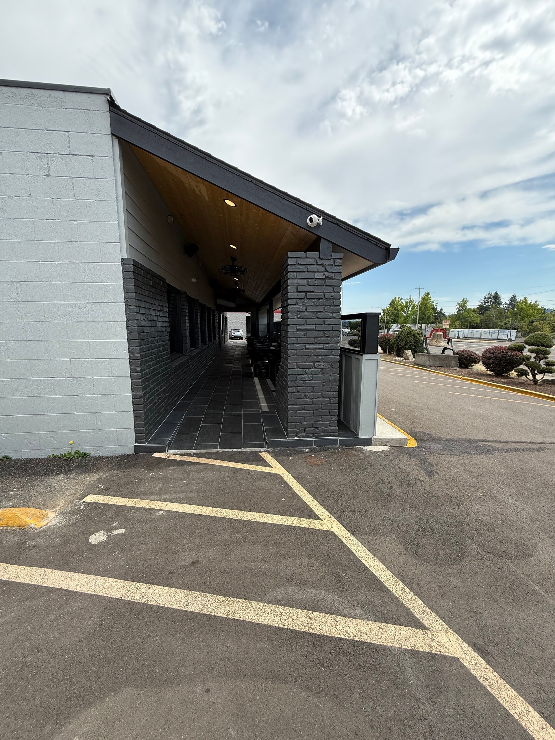 Exterior of a building with a covered walkway, featuring grey stone accents and accessible parking lines.