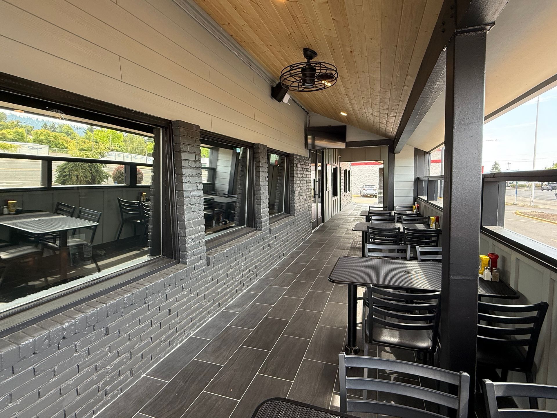 Outdoor restaurant patio with black tables, chairs, and grey brick wall.