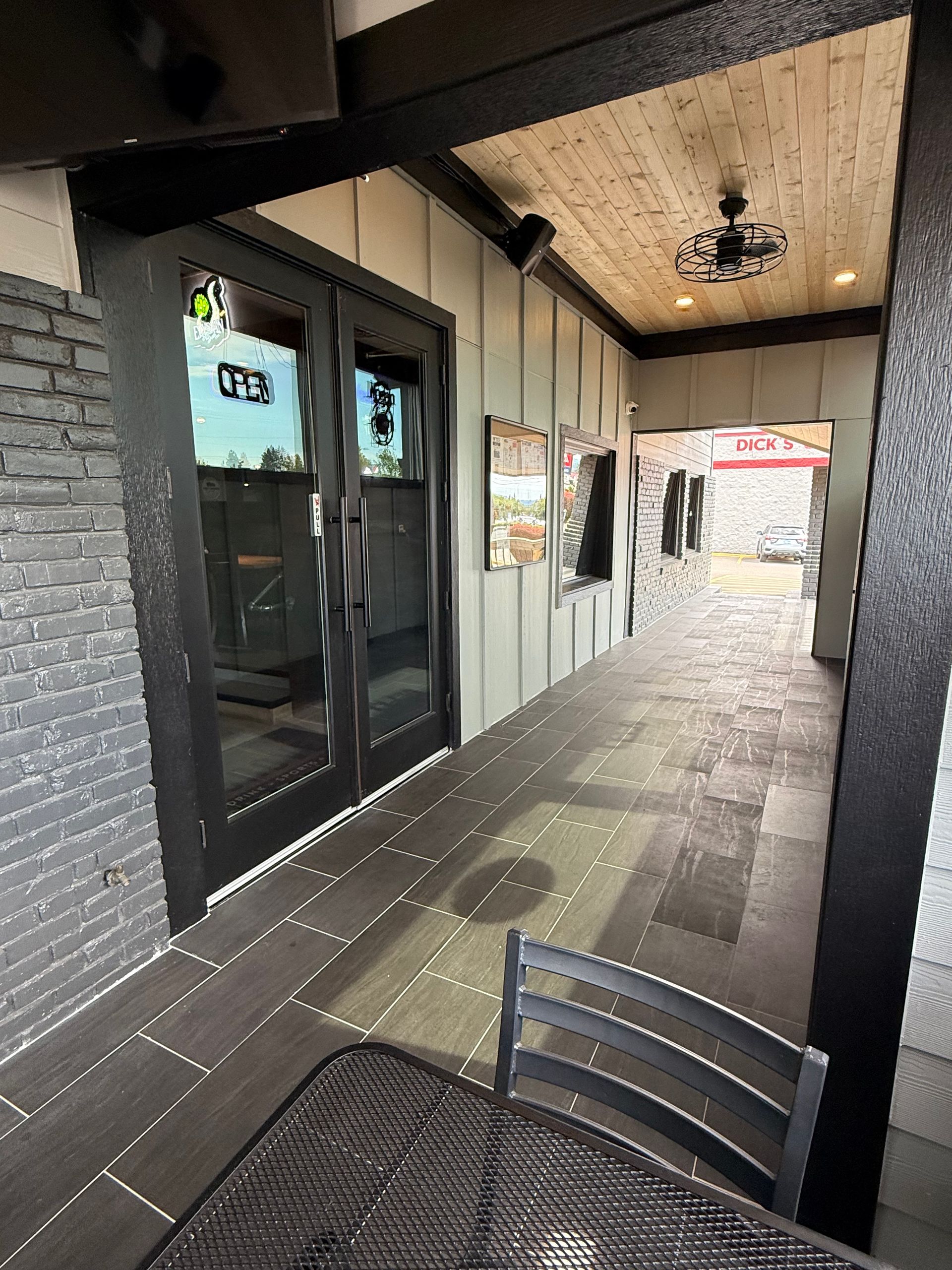 Outdoor restaurant patio with a black metal table and chairs, a walkway with doors, and a ceiling fan.