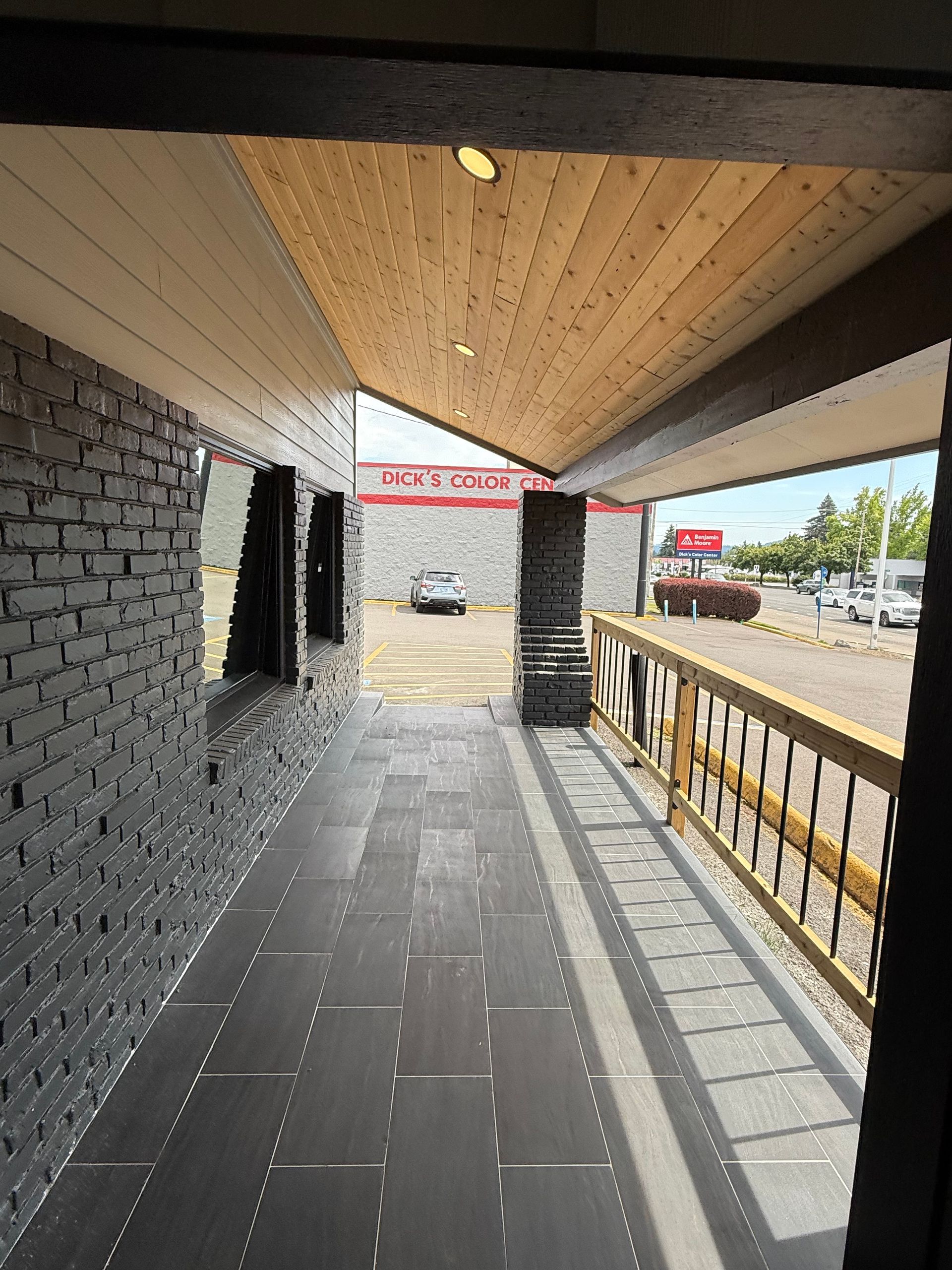 A covered outdoor walkway with gray brick, wooden ceiling, and a view of a parking lot.
