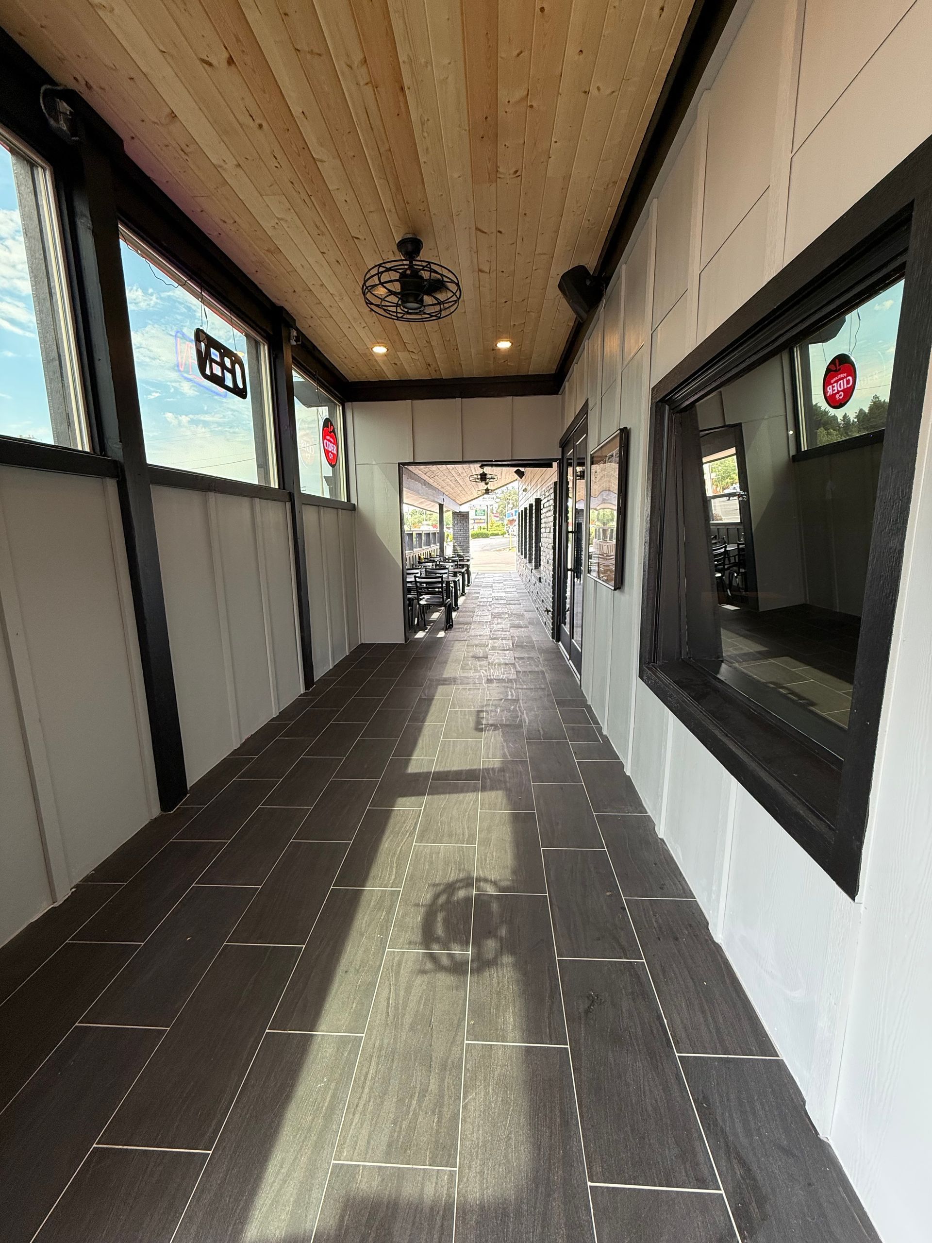 Narrow, dark hallway with wood ceiling and floor, windows, and a doorway at the end.
