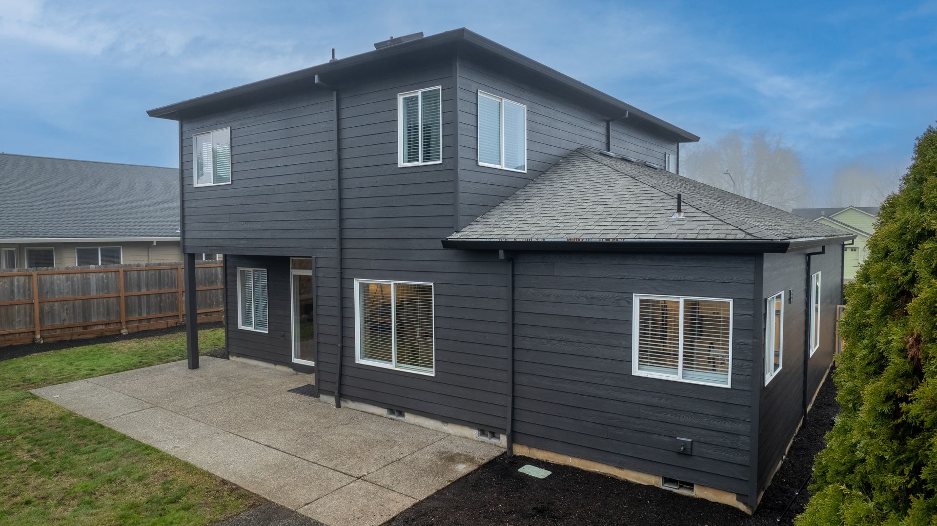 Dark gray two-story house with white-trimmed windows, patio, and green lawn.