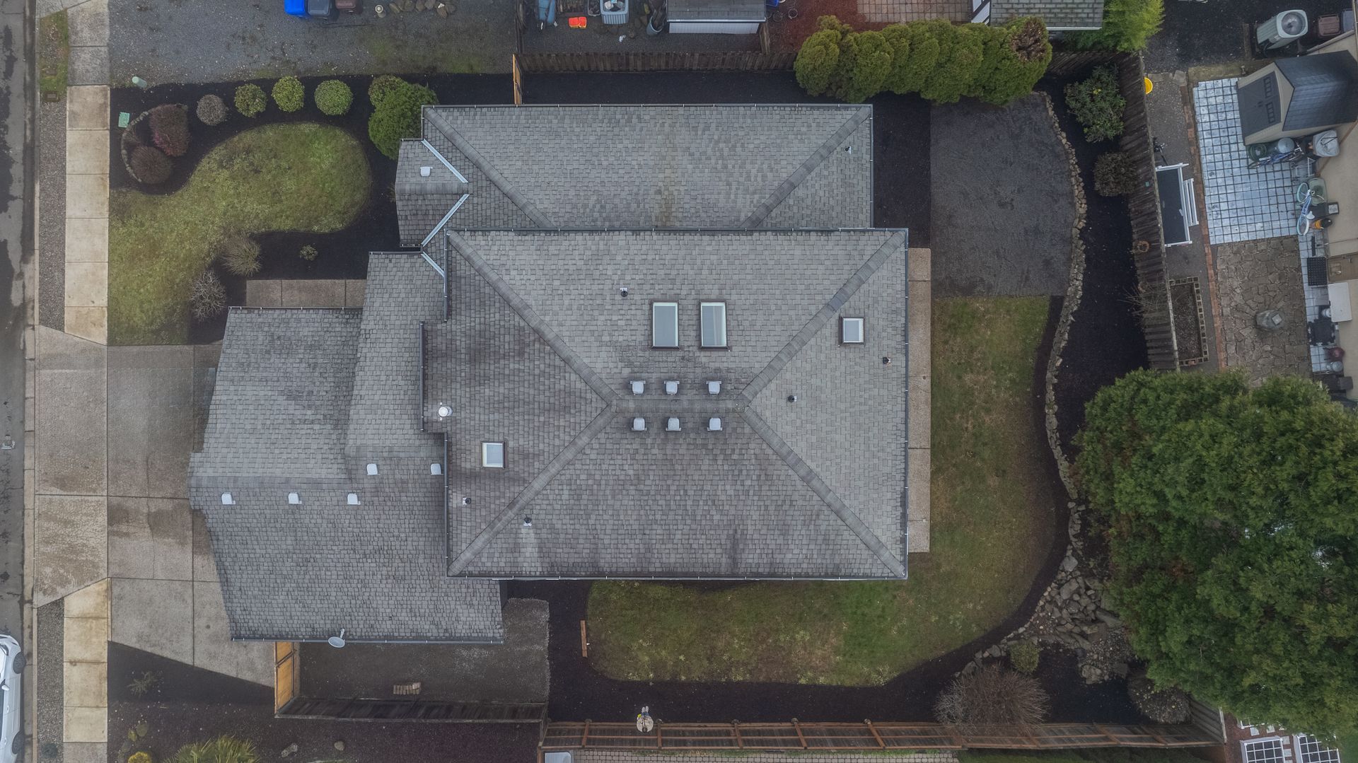 Overhead view of a house with a gray roof, surrounded by a lawn and garden beds with greenery.